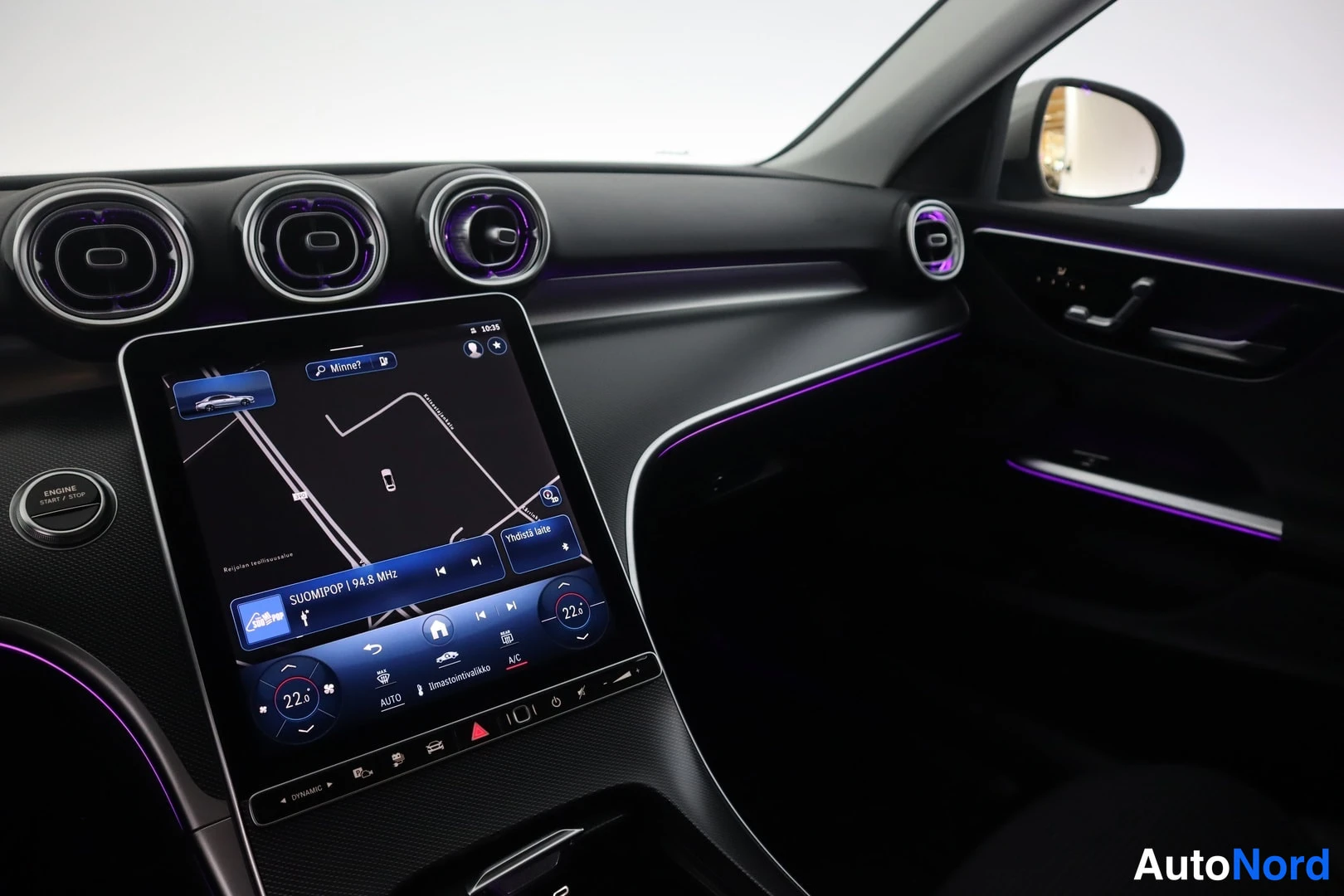 Ohjaamo: Interior shot of the dashboard with a central infotainment screen displaying navigation and radio. The climate control interface is visible on the screen, along