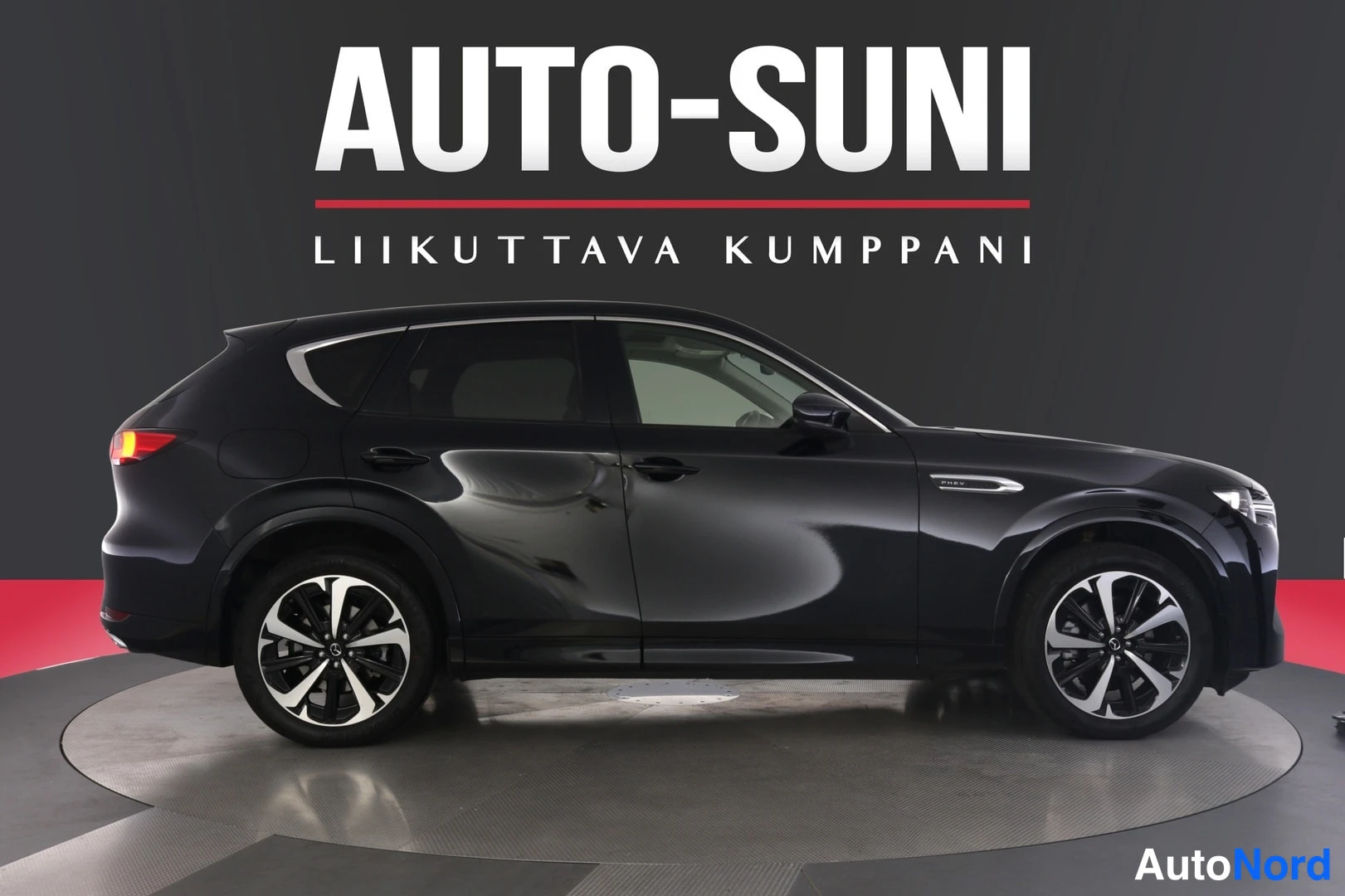 Sivulta: Sivukuva mustasta Mazda CX-60 -maasturista myyntihallin pyörivällä alustalla.