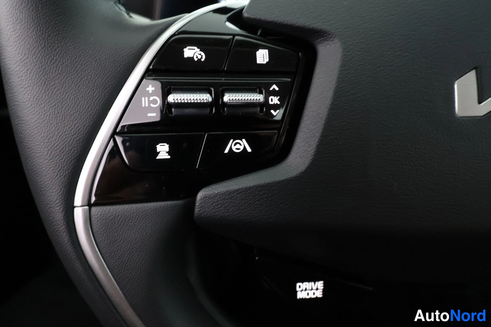 Yksityiskohta: Steering wheel control buttons visible including cruise control symbols (+/-), a display scroll button, and lane assist icon.