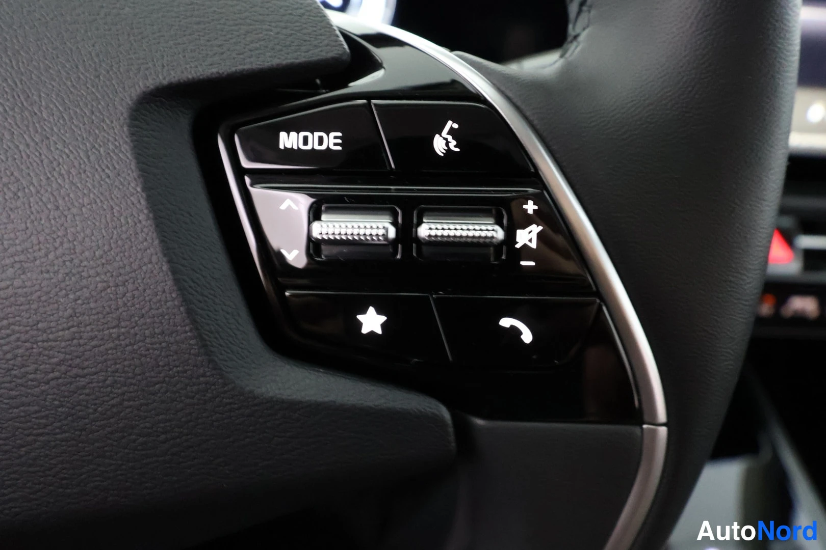 Yksityiskohta: Steering wheel controls showing MODE button, voice command symbol, volume rocker buttons, star favorite button, and phone call answer/end buttons.