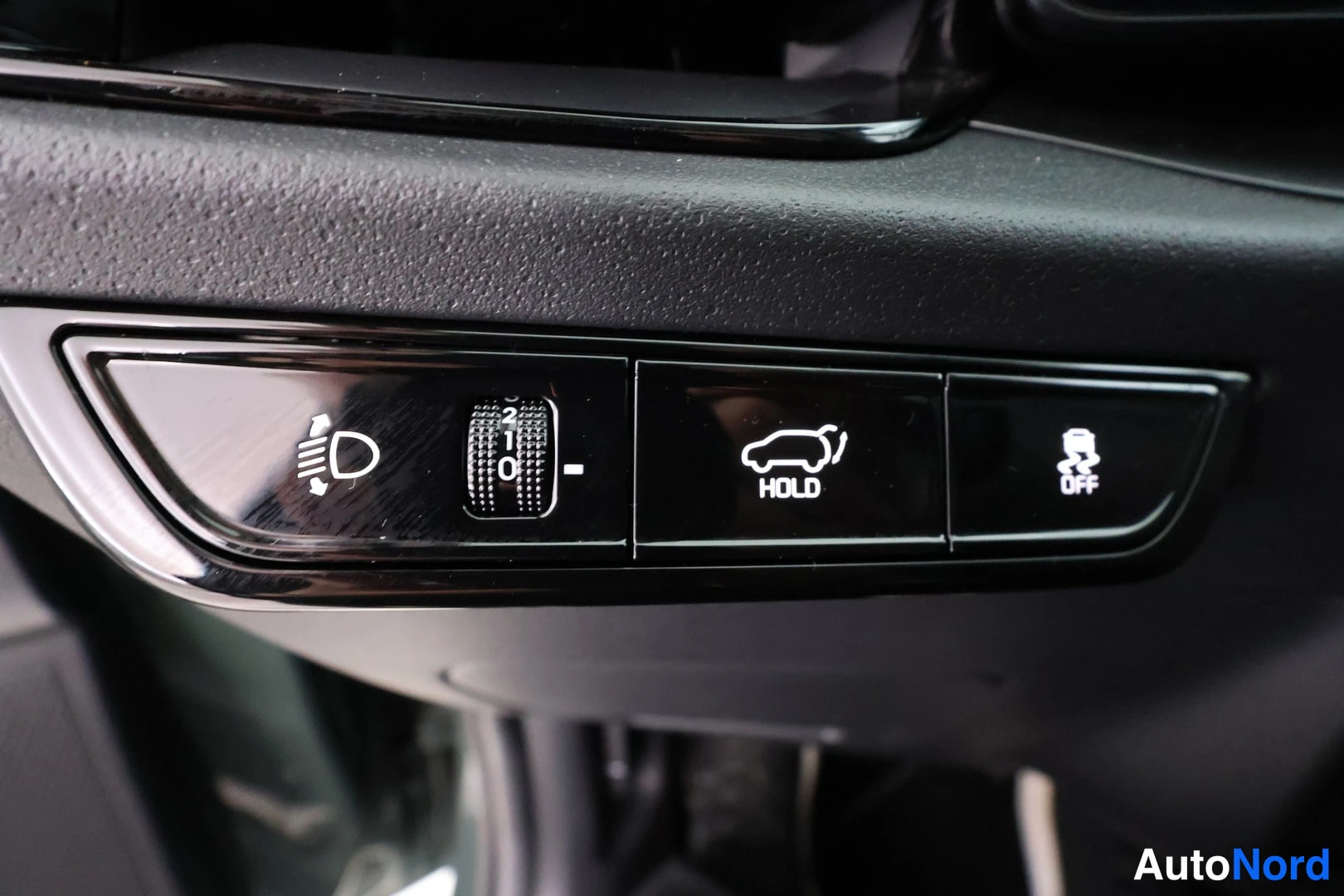 Yksityiskohta: Close-up of the instrument panel control panel showing buttons for Hill Hold Control (HOLD) and Traction Control Off, next to a headlight leveling dial.
