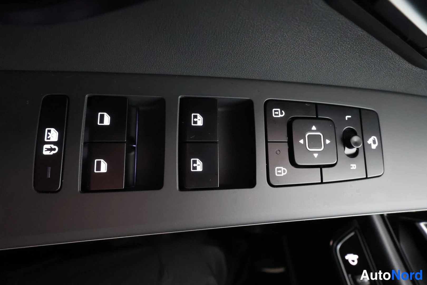 Yksityiskohta: Close-up of the driver's door armrest showing window switches and electronic mirror adjustment controls.