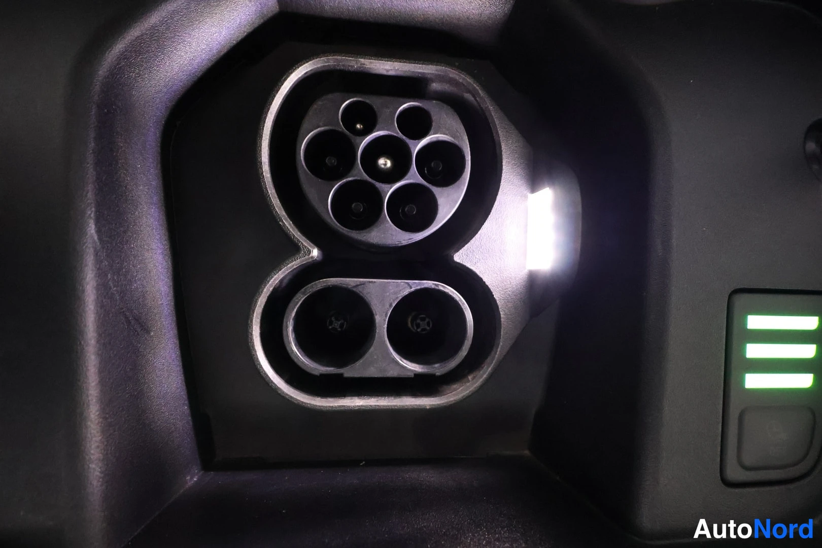 Yksityiskohta: Close-up of an electric charging socket with Type 2 connectors and an illuminated green indicator light.