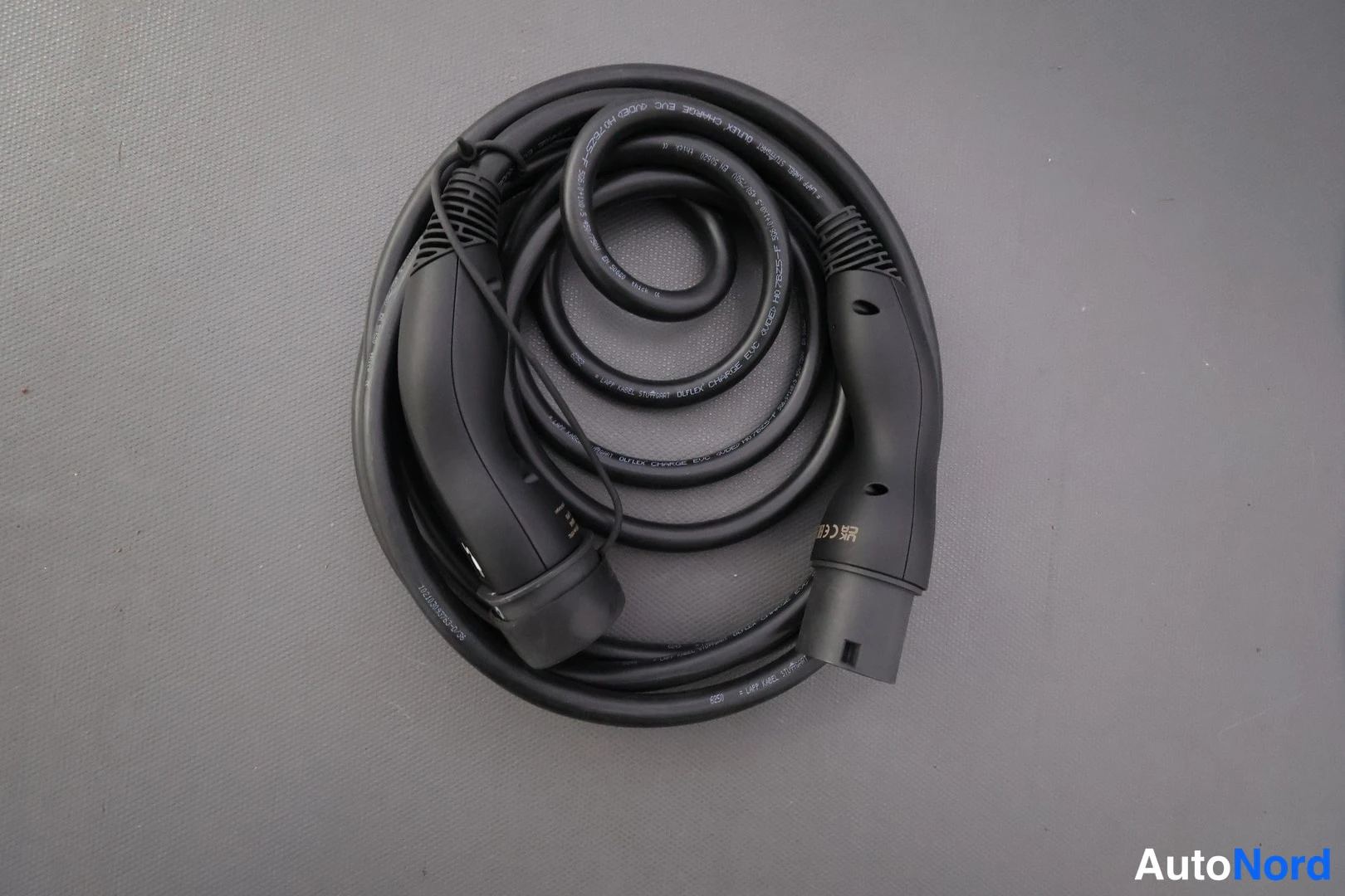 Muu: A coiled black charging cable lying on a gray textured surface.