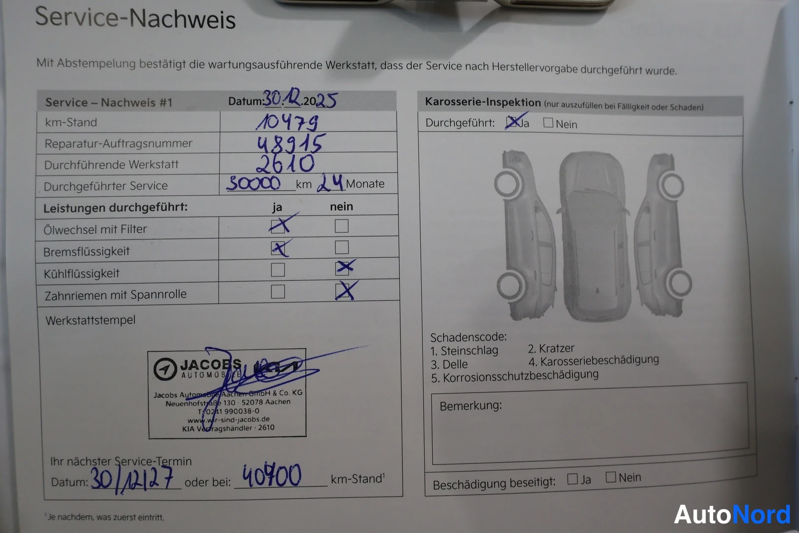 Asiakirja: Close-up photograph of a stamped service booklet page in German (Service-Nachweis) with handwritten maintenance records for mileage up to 40,700 km.