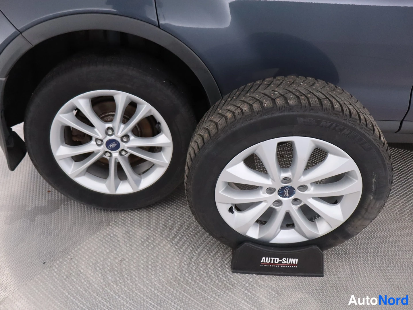 Yksityiskohta: Renkaita ja Ford-merkkisiä hopeavanteisia pyöriä tummansinisenä autona.
