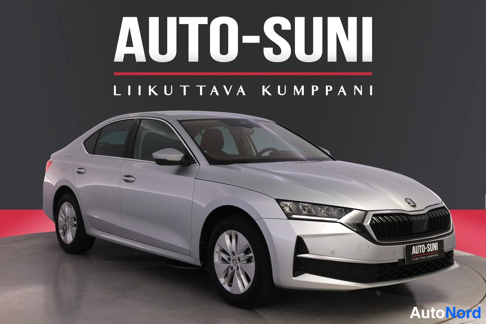 Etuviisto, nokka oikealle: Silver Skoda Octavia sedan in a front three-quarter view on a showroom turntable. The image includes large text 'AUTO-SUNI' and the Finnish slogan 'LIIKU
