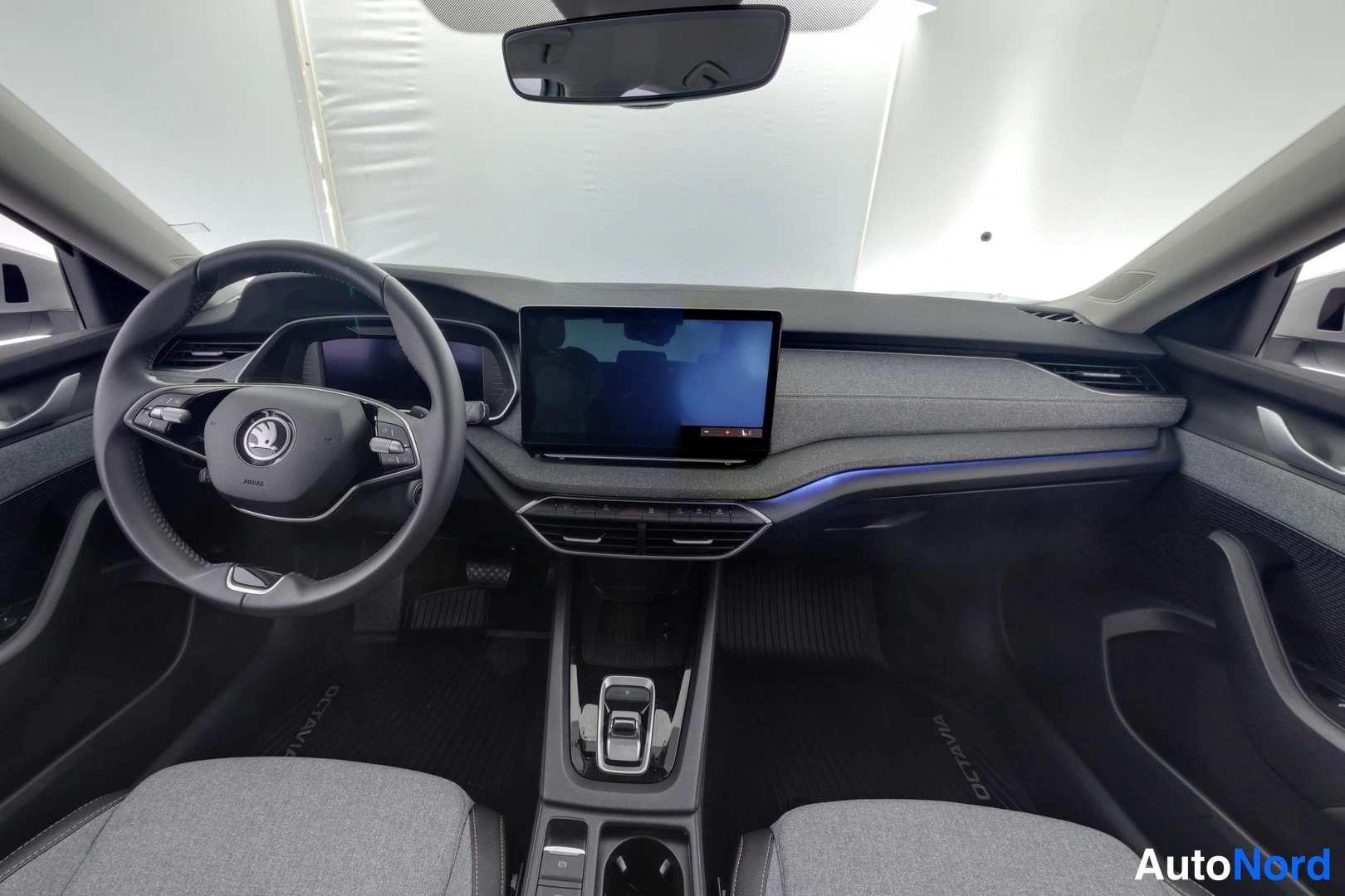 Ohjaamo: Interior dashboard view showing the steering wheel with controls, digital instrument cluster, central infotainment screen, gear selector, air vents and fabric f