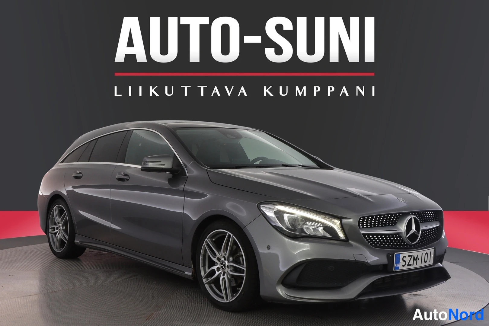 Etuviisto, nokka oikealle: Grey Mercedes-Benz Shooting Brake at a three-quarter front angle with grille and right flank visible on showroom turntable