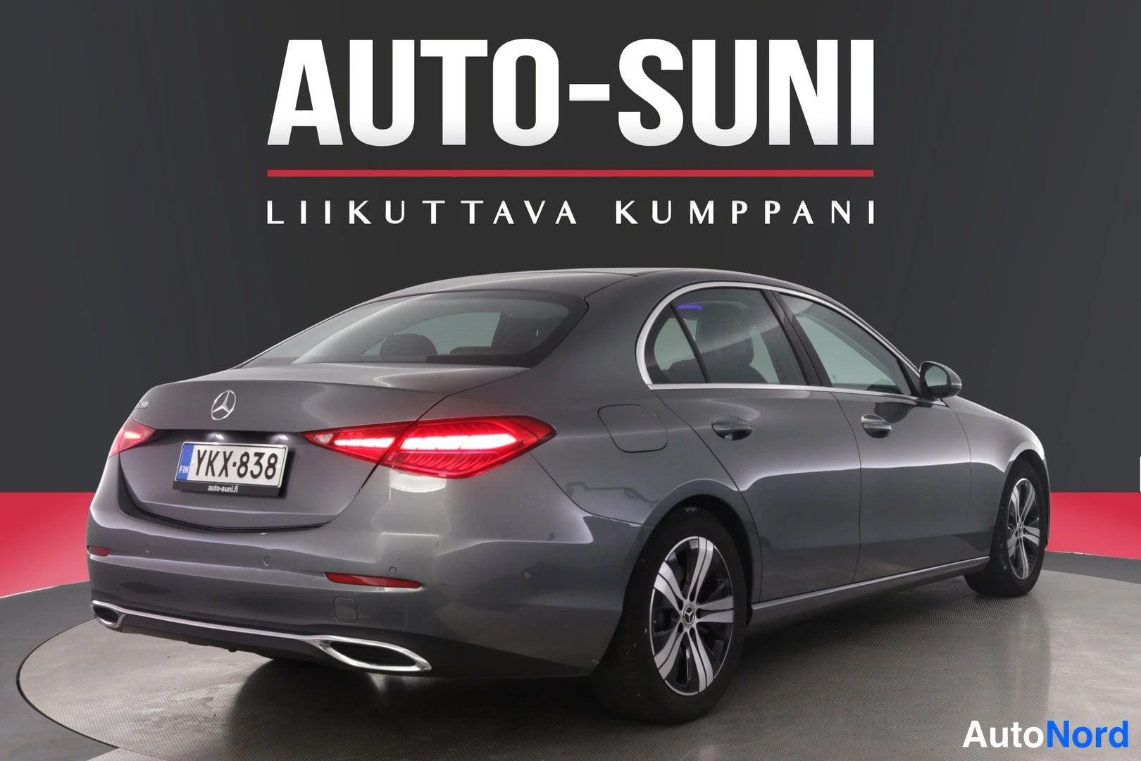 Takaviisto: Harmaan Mercedes-Benz C-sedan takaviisto vasemmalta, sytytetyt takavalot, rekisteritunnus, Auto-Suni-studio.