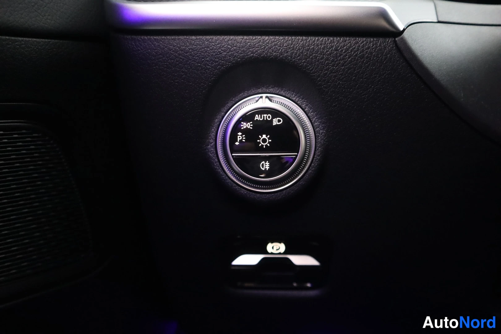 Yksityiskohta: Ajovalokytkimen automaattiasento AUTO ja pysäköintiassistentin painike mustassa kojelaudassa.