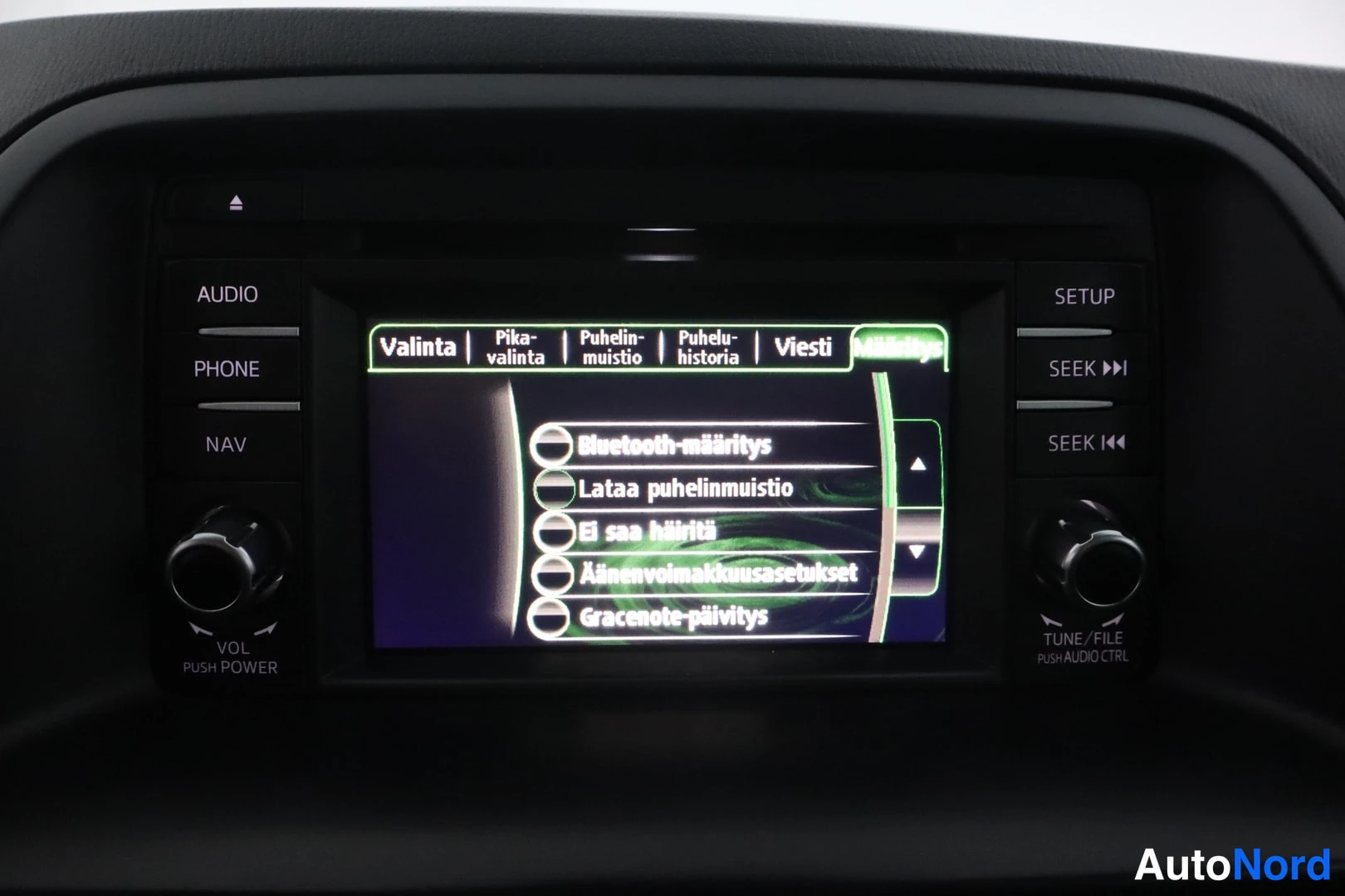 Yksityiskohta: Auton kesk konsolin infotainment-näyttö suomenkielisellä valikolla (Bluetooth-määritys, Lataa puhelinmuistio ym.), AUDIO/PHONE/NAV- ja SETUP/SEEK-painikkeet sek