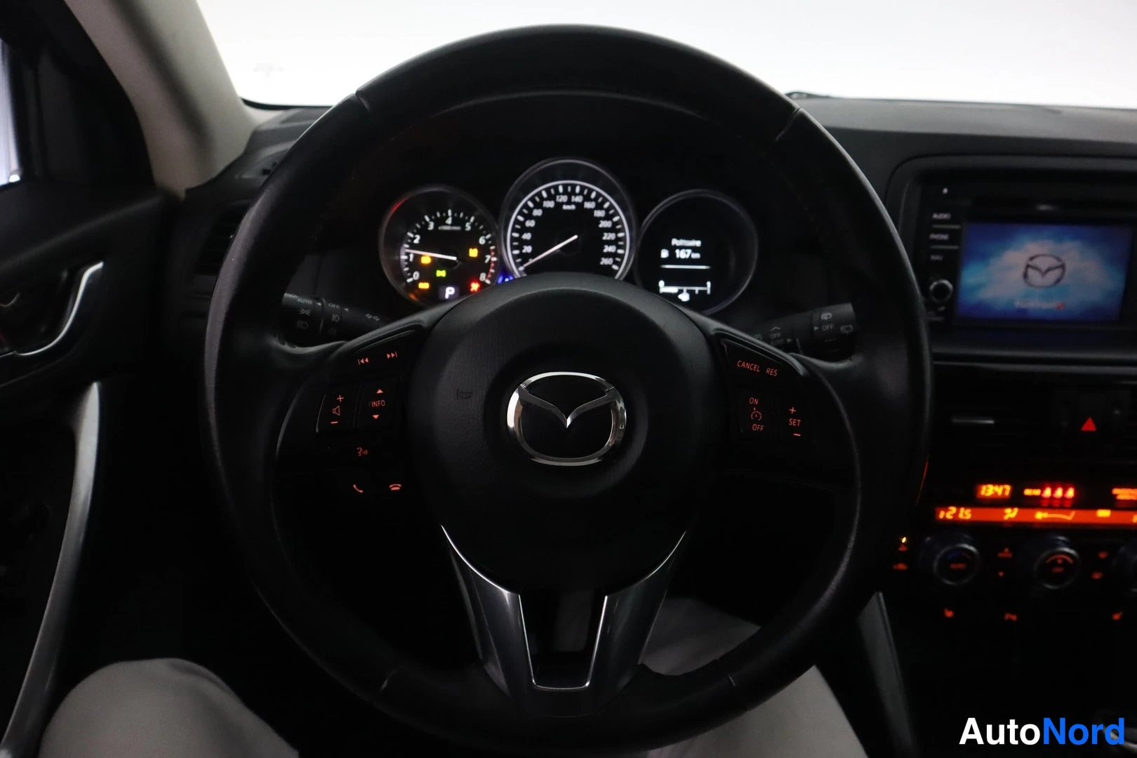 Edestä: Ohjauspyörä ja kojelauta, joiden keskellä Mazda-merkki ja merkkivalot.