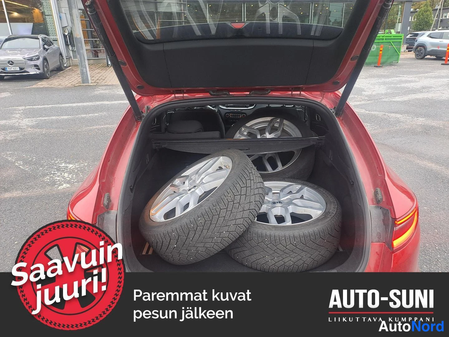 Takaa: Auton tavaratila auki; tilassa kolme vaihtopyörää hopeavanteilla ja suojaverho irrotettuna. Kuvassa myyjän tekstillisiä lisäyksiä.