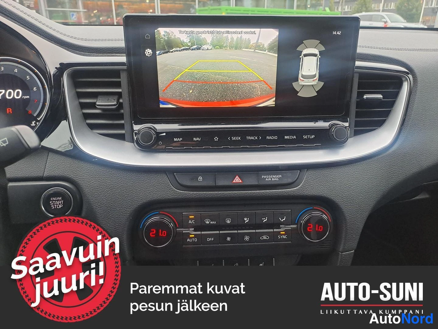 Muu: Infotainment-näytöllä peruutuskameran kuva parkkipaikasta kaariviivoineen ja ympärsönäkymägrafiikka; keskikonsolin ilmastointipaneeli näkyy alla.