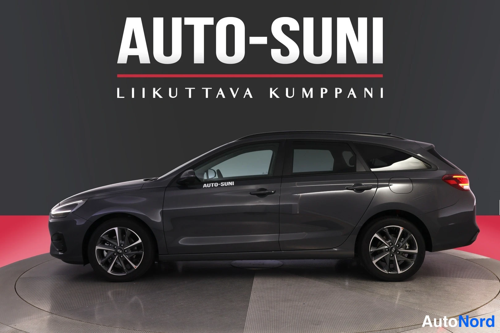 Sivulta: Hyundai i30 Wagon -farmariauto sivusta etviistossa, tummanharmaa kori ja tummat kevytmetallivanteet studiotaustaa vasten.