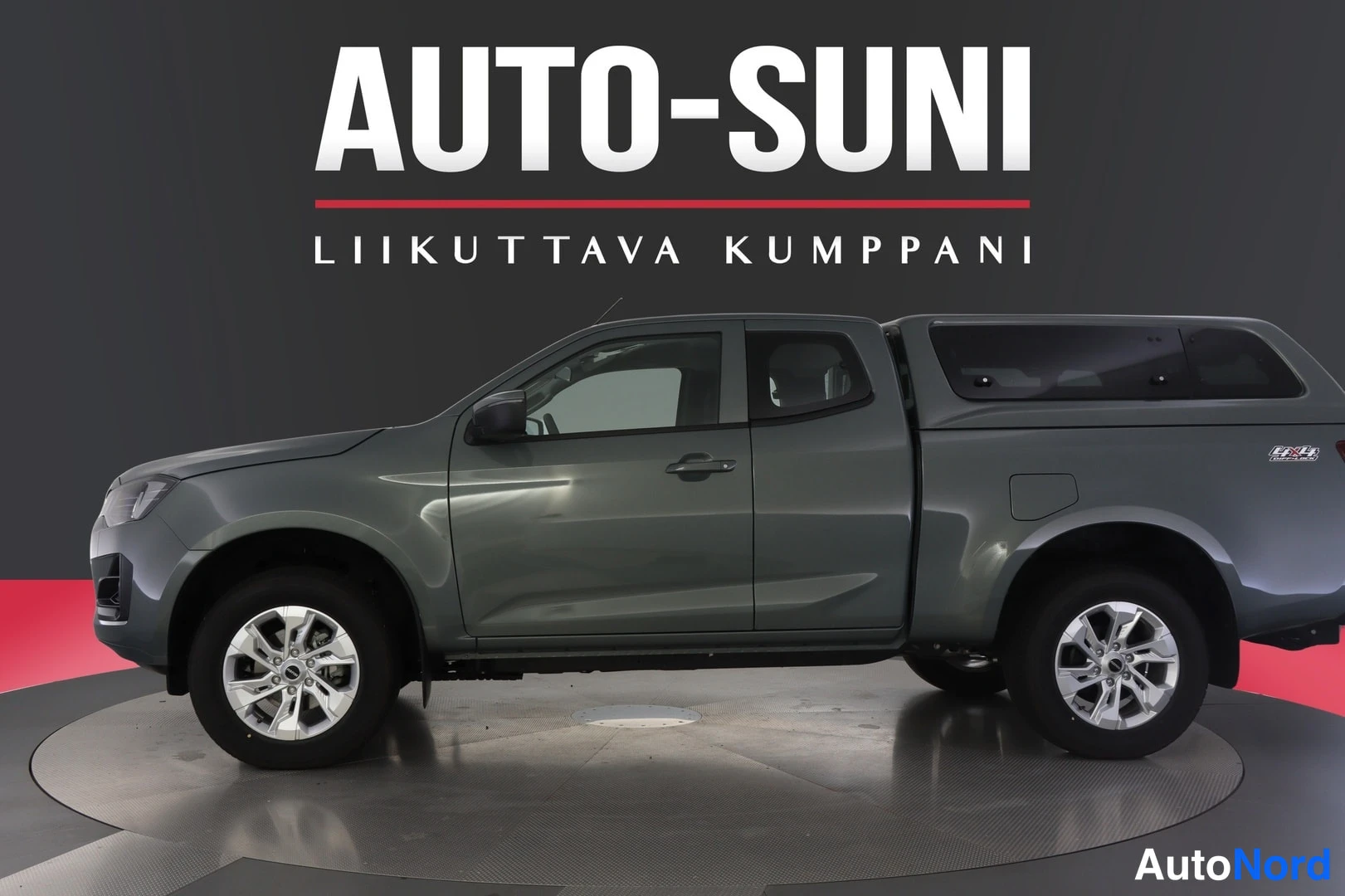 Sivulta: Harmaa avolava-auto näkyy vasemmasta etukulmasta studioympäristössä, lisäkorin peittämä lavakansi ja hopeiset vanteet.