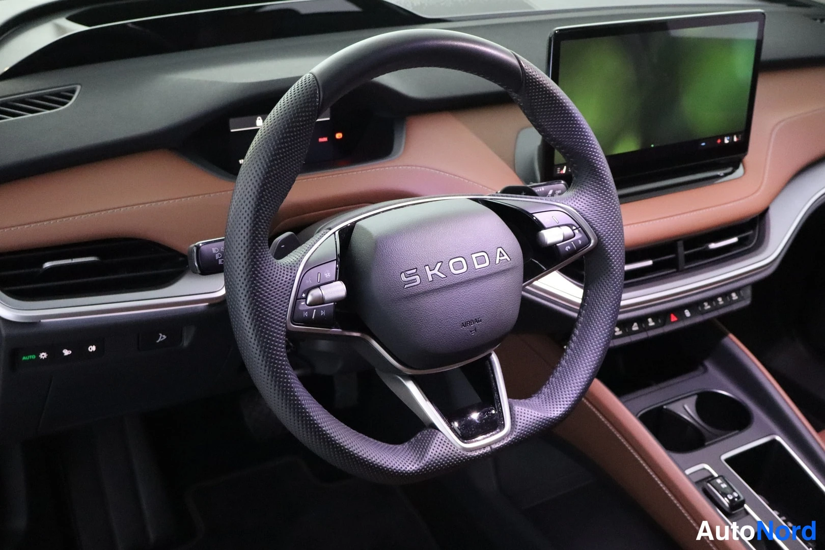 Muu: Skoda-merkkinen ohjauspyörä mustalla nahalla, taustalla ruskea kojelauta ja keskellä suuri näyttö.