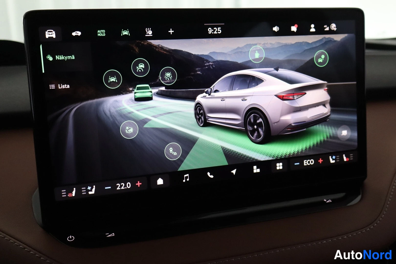 Yksityiskohta: Infotainment-näytön Näkymä-valikko ajoneuvoturvallisuus- ja kulmausaputoiminnoille, autokuva mäkisessä maisemassa.