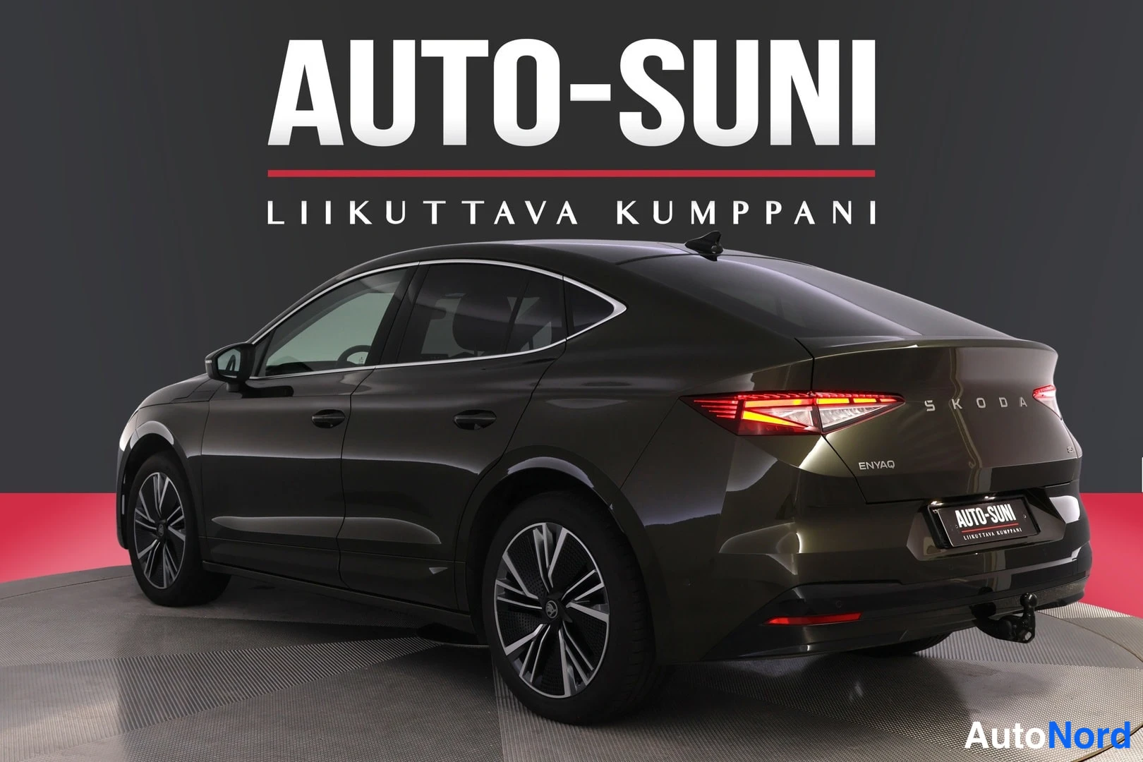 Takaviisto: Skoda Enyaq takakulmasta oikealta; ENYAQ-merkintä ja tummanruskea kori näkyvät studioympäristössä.