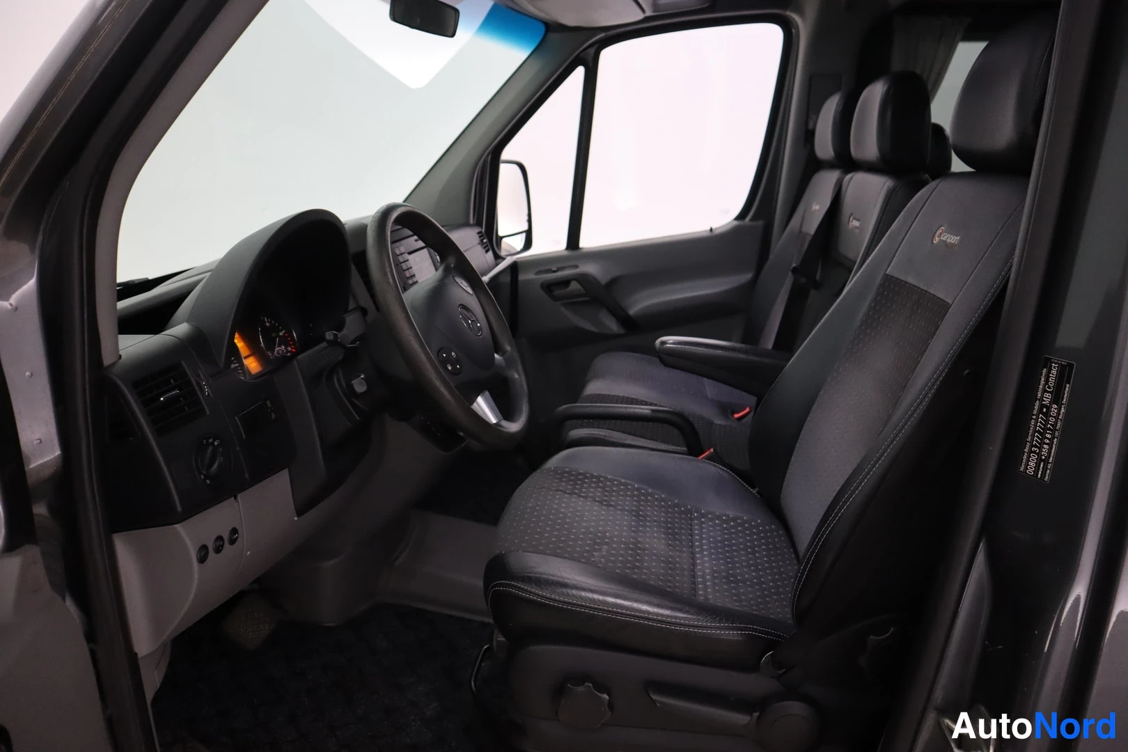 Muu: Sisäkuva kuljettajan puolelta: Mercedes-Benzin ohjaamo, ratissa Mercedes-merkillä, mustat tekstiili-istuimet ja kojelaudan merkinnät 'Comfort'.
