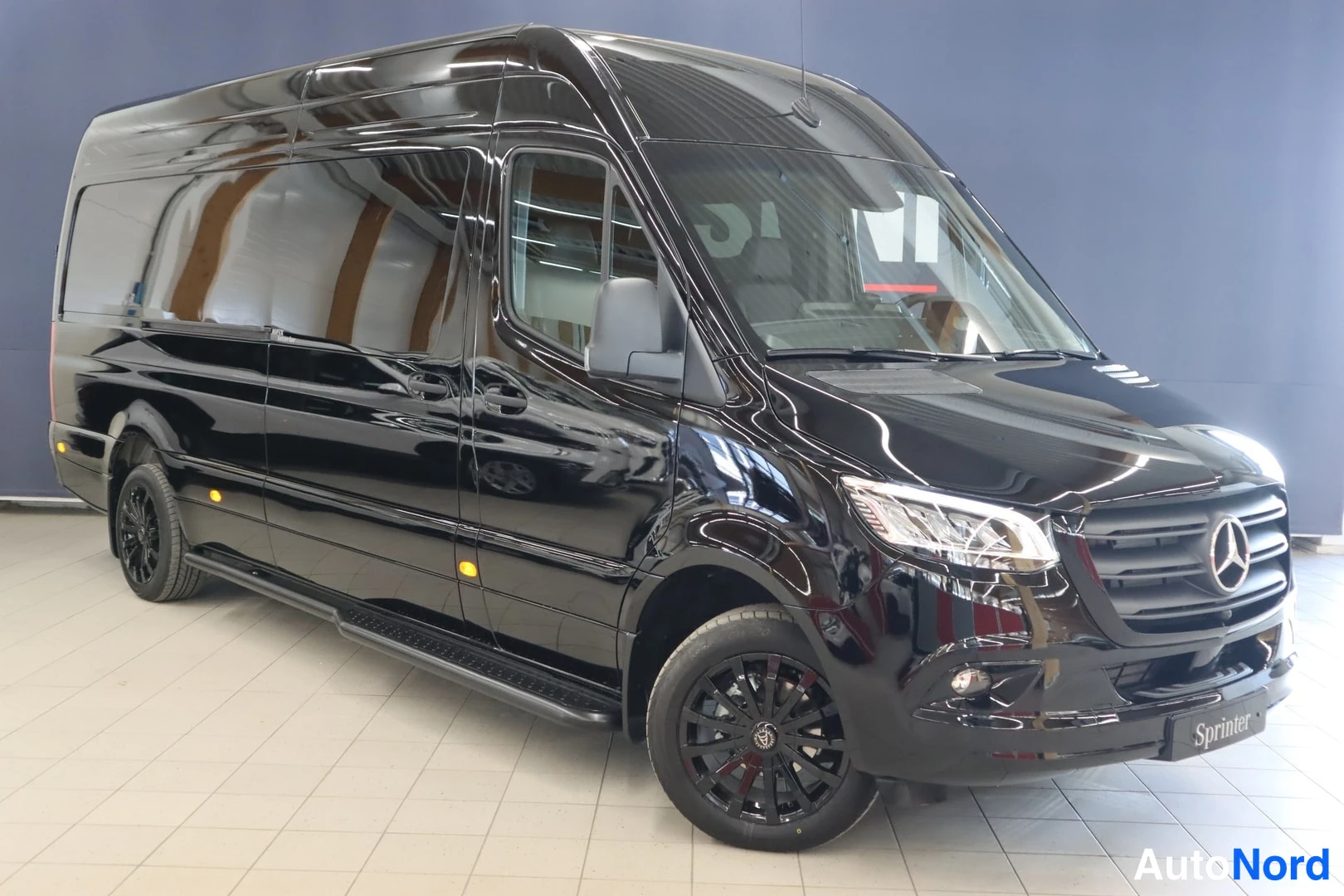 Etuviisto, nokka oikealle: Musta Mercedes-Benz Sprinter -pakettiauto etuviistosta oikeaan kulmassa, näkyvät mustat vanteet ja sivuponnellus.