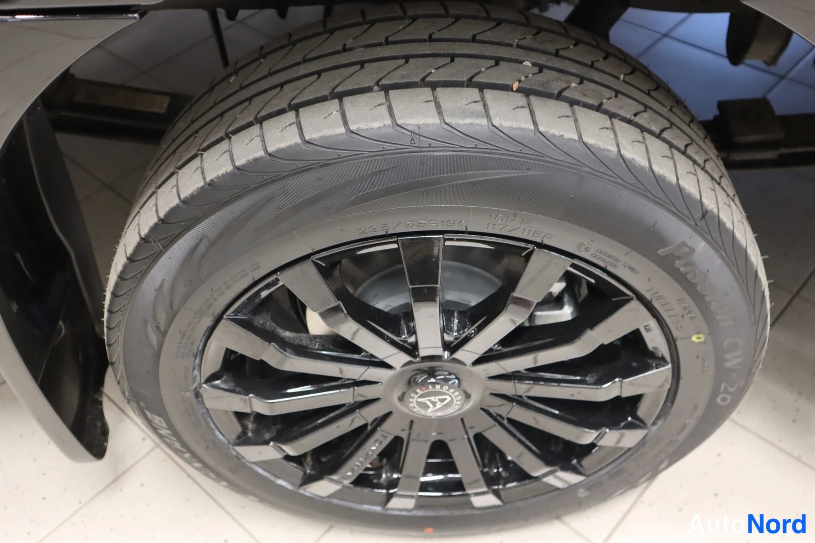Yksityiskohta: Musta monipuolinen kevytmetallivanne mustalla rungolla, renkaankyljessä näkyvät mitat 235/55R19 111W M+S ja merkintä Passion CW-20.