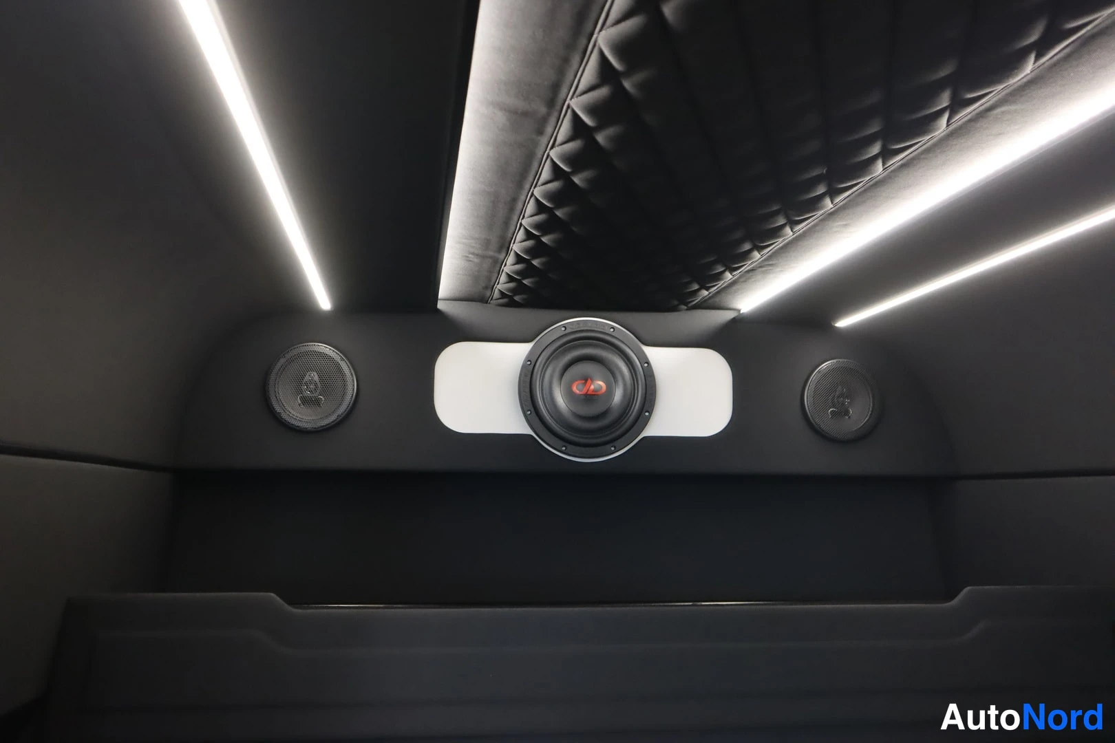Yksityiskohta: Kattopaneeli, jossa keskellä iso subwoofer-kaiutin ja sivuilla kaksi pienempää kaiutinta, LED-valonauhat.