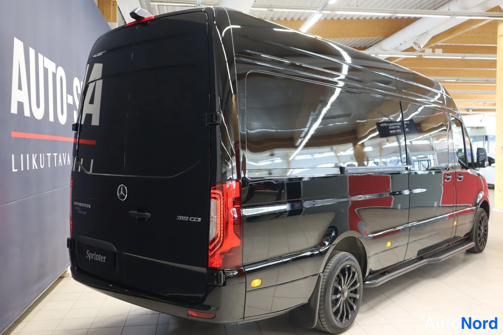 Takaviisto: Mustan Mercedes-Benz Sprinter -pakettiauton takaosa ja vasen sivu näkyvät sisätiloissa.