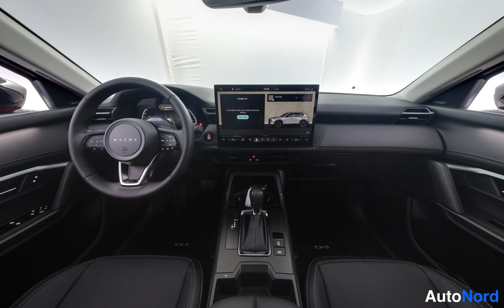 Muu: Auton ohjaamo: Mazda-ohjauspyörä, keskikonsoli ja infotainment-näyttö, tummat penkit.