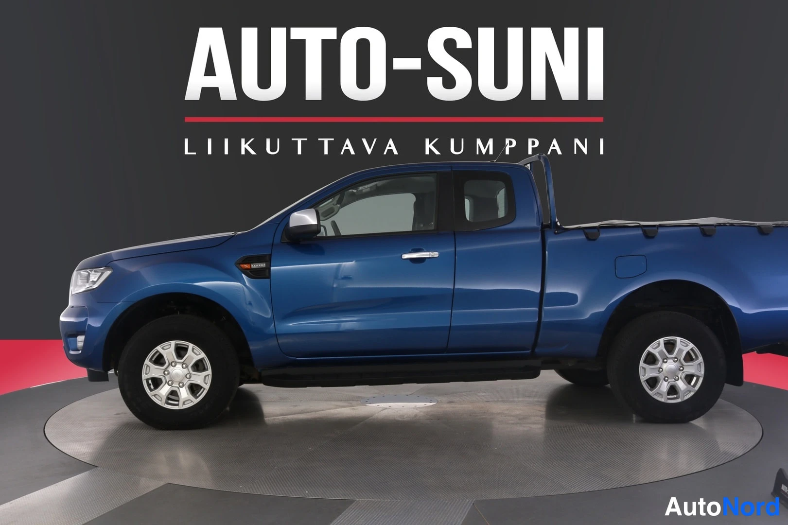 Sivulta: Sininen Ford Ranger Super Cab -avolava täryauto sivulta vasemmasta etukulmasta studioturntablella, koko kori ja alumiinivanteet näkyvät, taustalla.Auto