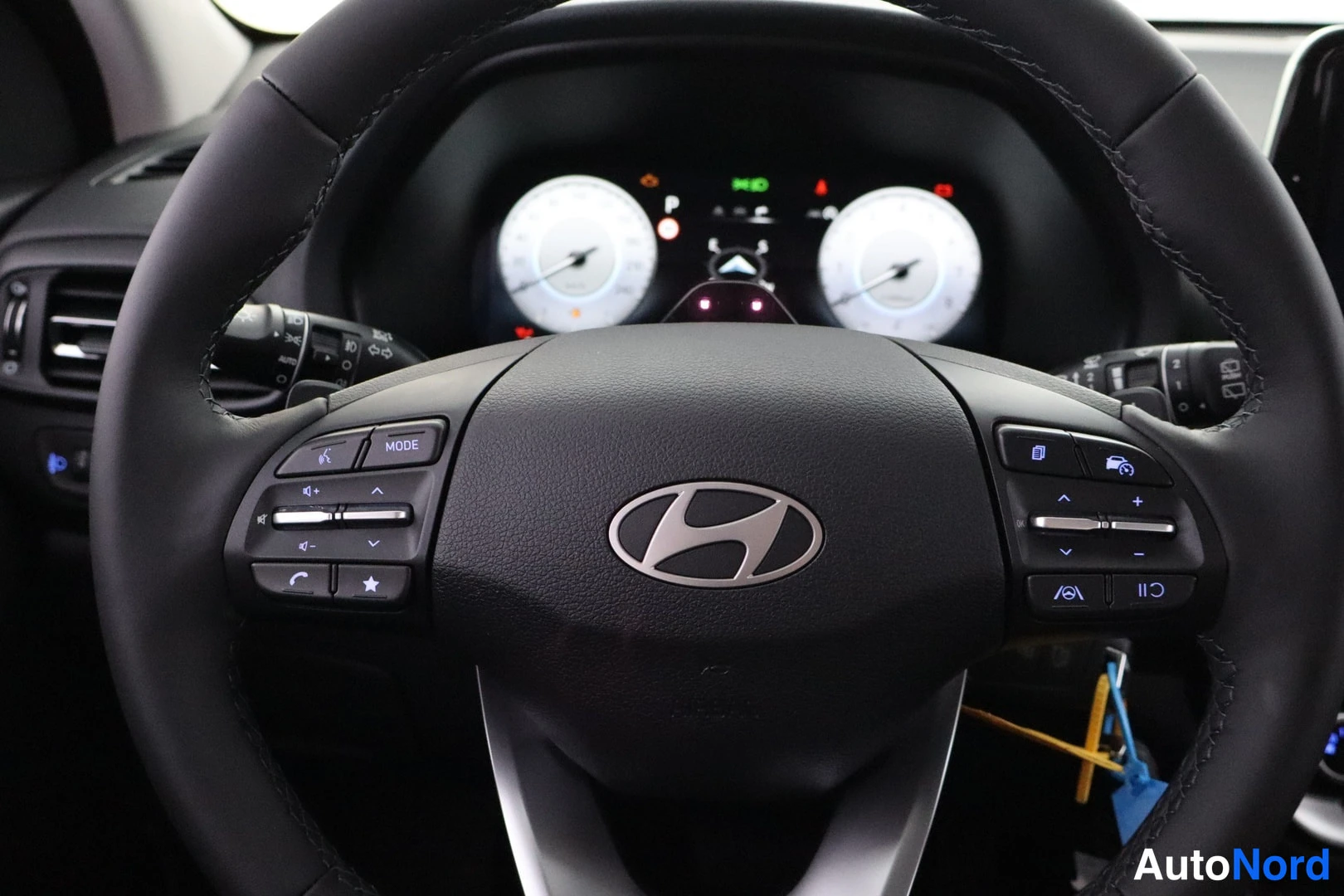 Yksityiskohta: Ohjauspyörä Hyundai-merkillä, monitoiminapeilla molemmin puolin ja mittaristo taustalla.