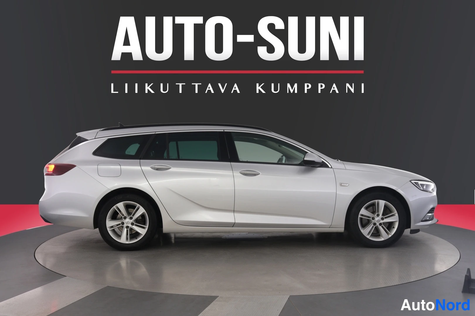 Sivulta: Hopeanvärinen farmariauto sivulta kuvattuna studioympäristössä, taustalla AUTO-SUNI LIIKUTTAVA KUMPPANI -teksti