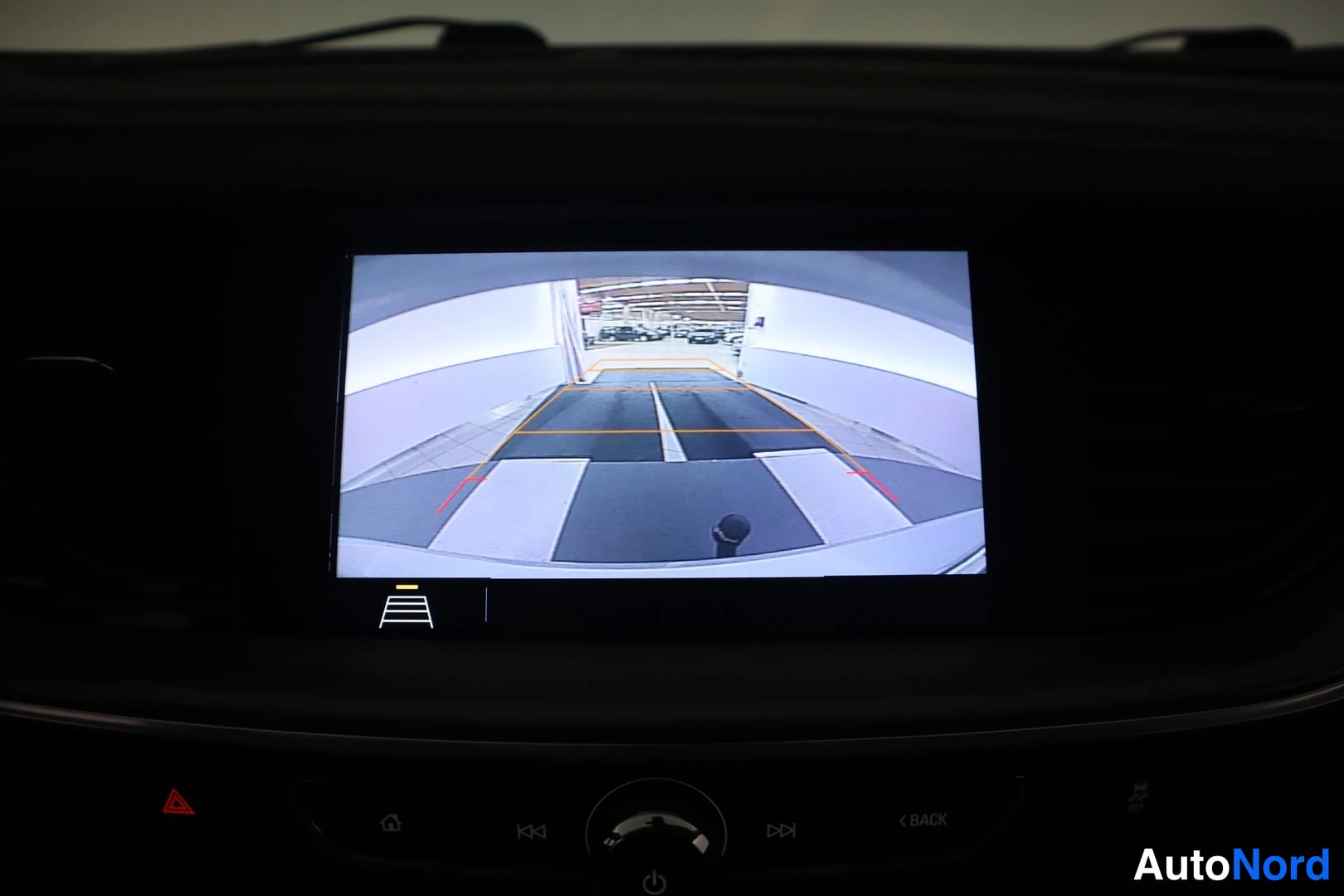 Muu: Infotainment-näyttö näyttää peruutuskameran kuvan pysäköintitutkan opastusviivoilla; näytön alla ovat kotipainike, kelausnäppäimet, pyöreä virta/volyymisäädin,