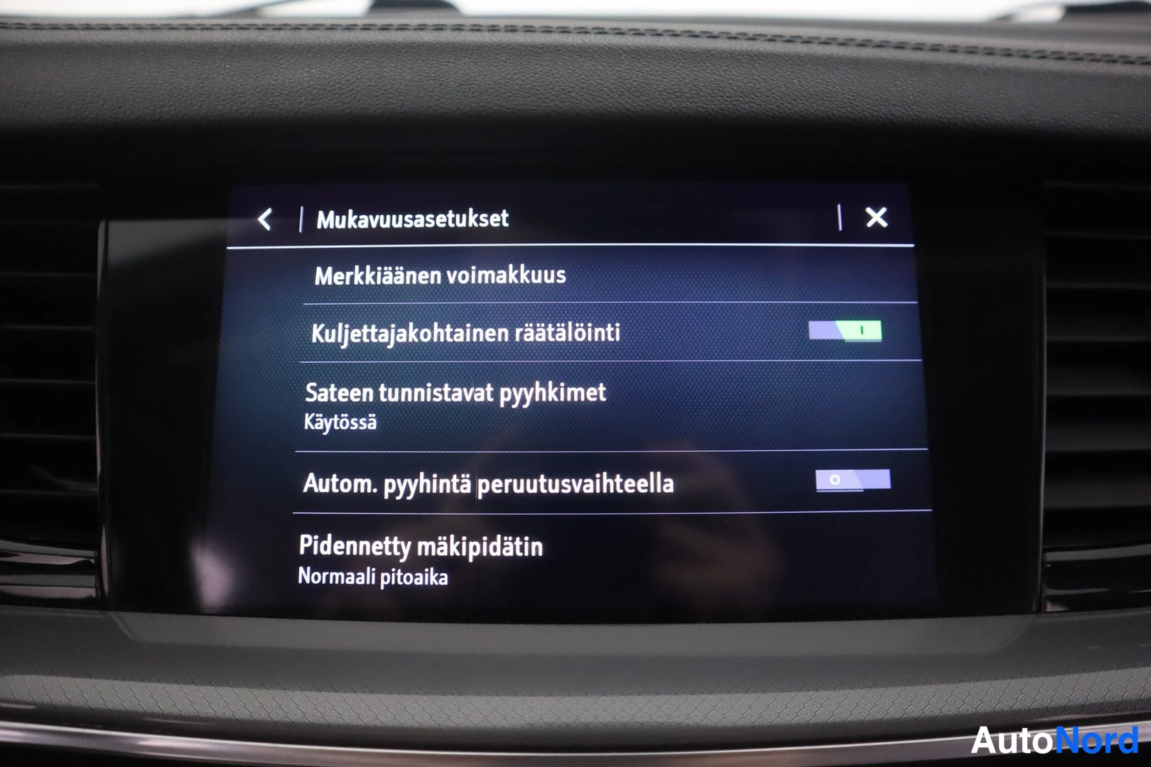 Yksityiskohta: Auton kojelaudan infotainment-näyttö, jossa Mukavuusasetukset-valikko mm. sateentunnistavista pyyhkimistä ja pidennetystä mäkipidättimestä.