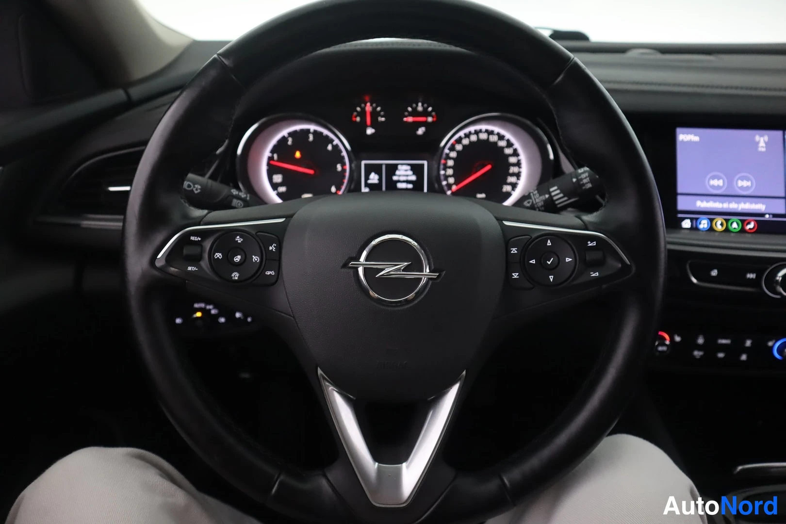 Muu: Opel-merkkinen ohjauspyörä monitoimipainikkeineen, taustalla kojelaudan mittarit ja multimedianäyttö.