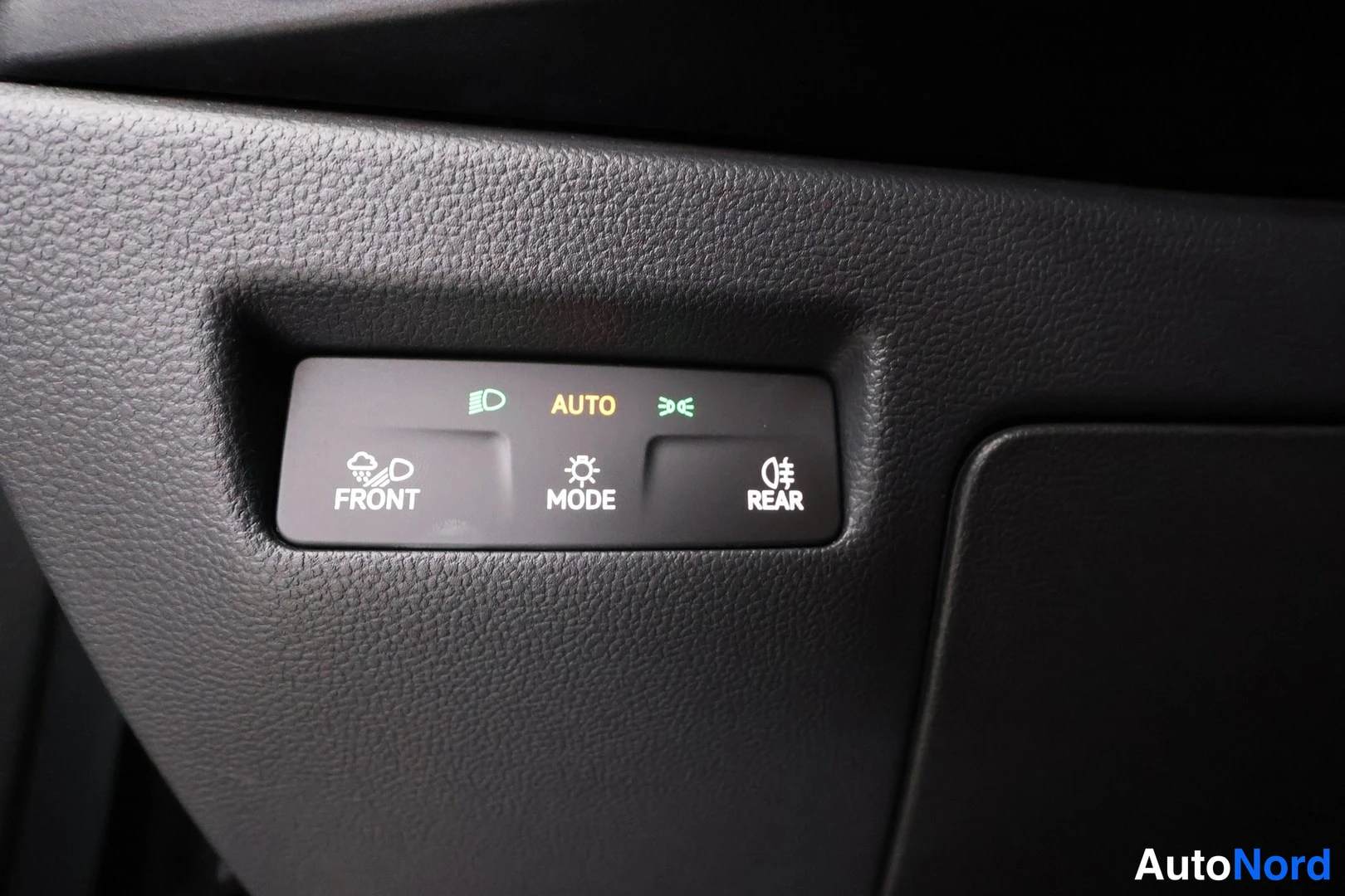 Yksityiskohta: Auton sisätilan välähdyssulku- ja sumuvalokytkinpaneeli: nappulat FRONT, MODE ja REAR sekä AUTO-merkintä.