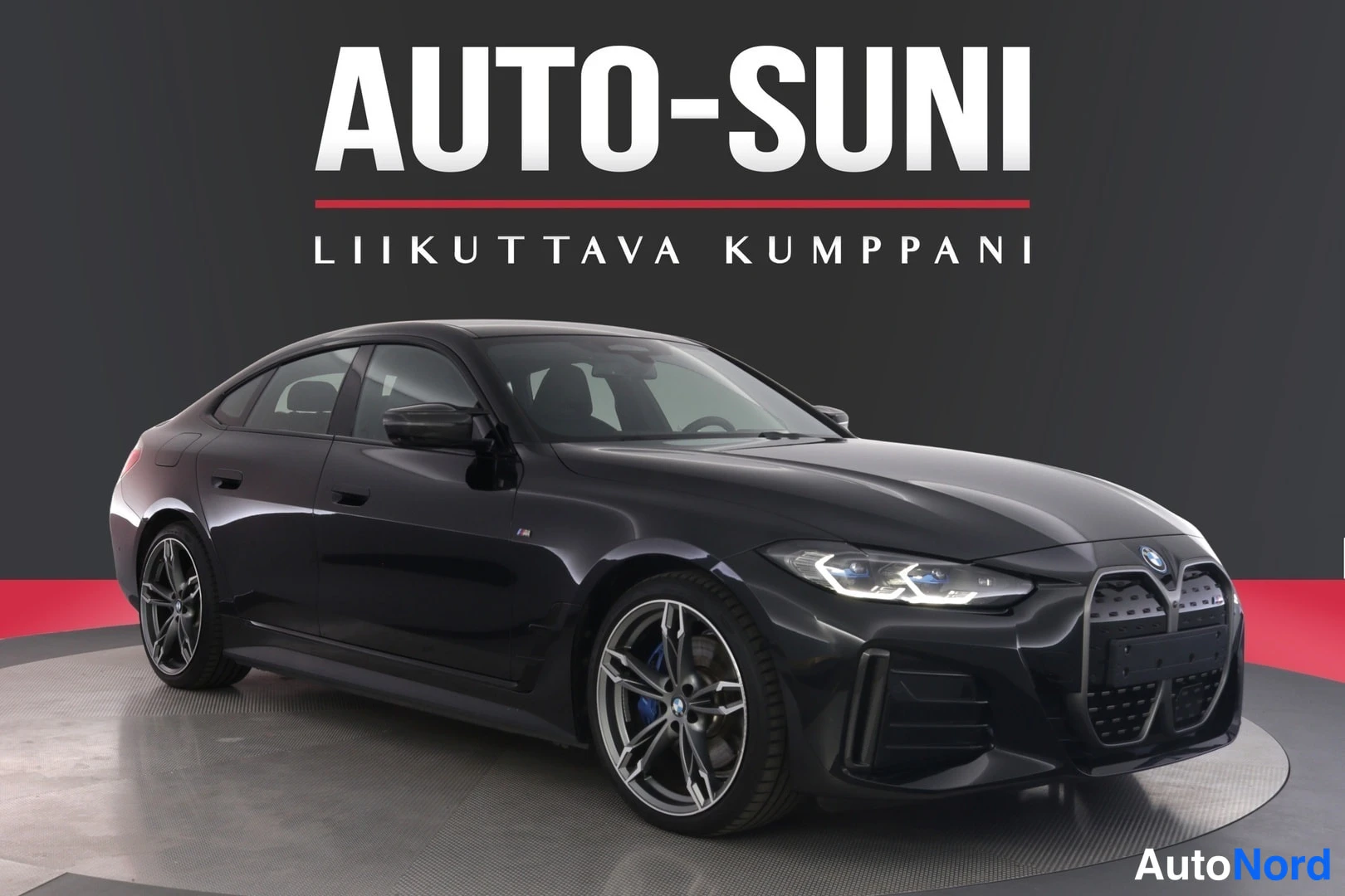 Etuviisto, nokka oikealle: Musta BMW i4 -sedan etuviisterechts kulmakuva studiosta, tumma tausta ja punainen lattia.