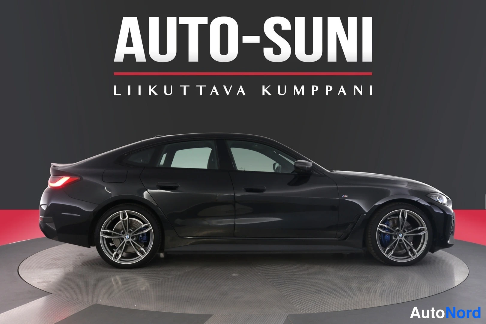 Sivulta: Musta BMW i4 -sedan sivuprofiili studiosta, tumma tausta ja punainen lattia.