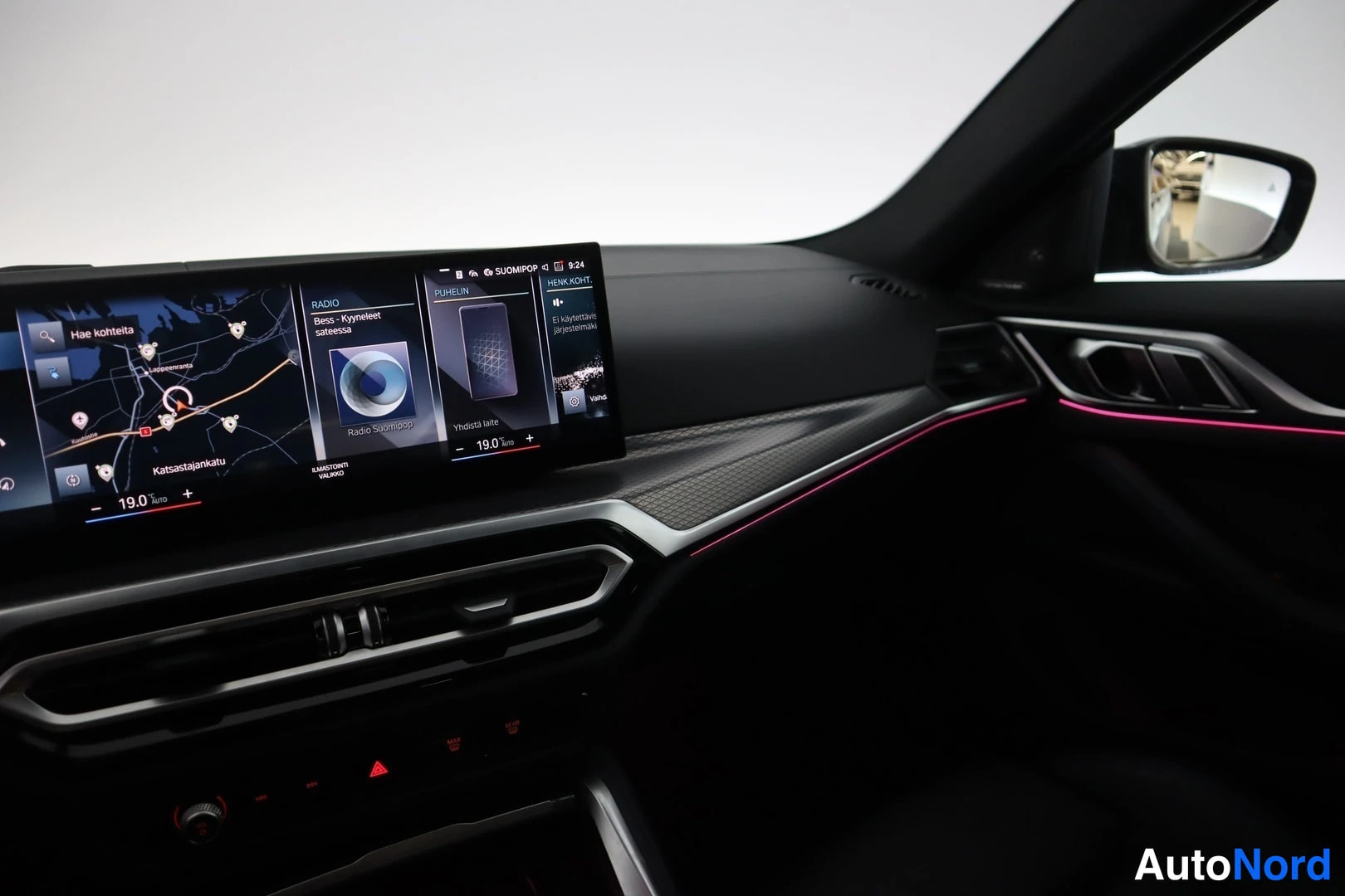 Yksityiskohta: BMW:n infotainment-näyttö kartta- ja radioikkunoilla, punainen ympäristövalaistus ja tumma mittaristo.
