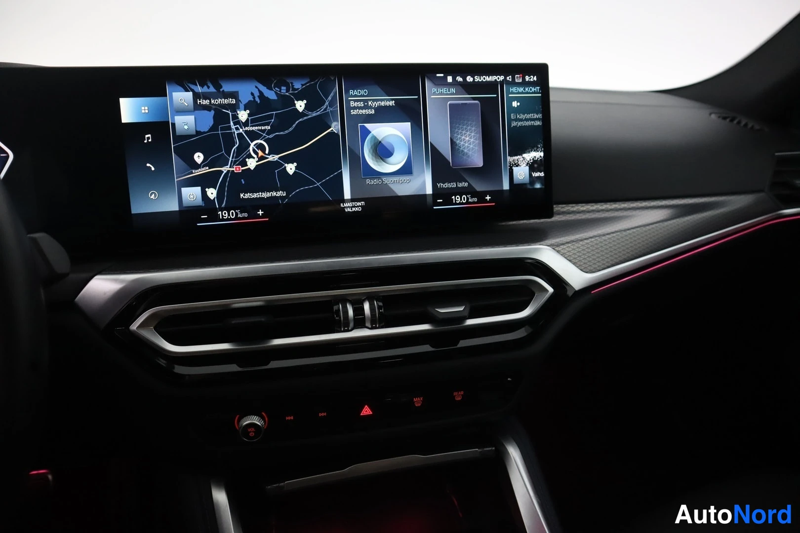 Yksityiskohta: BMW:n infotainment-näyttö kartta-, radio-, puhelin- ja HENK. KOHT. -ikkunoilla, punainen ympäristövalaistus ja sumuvalot.
