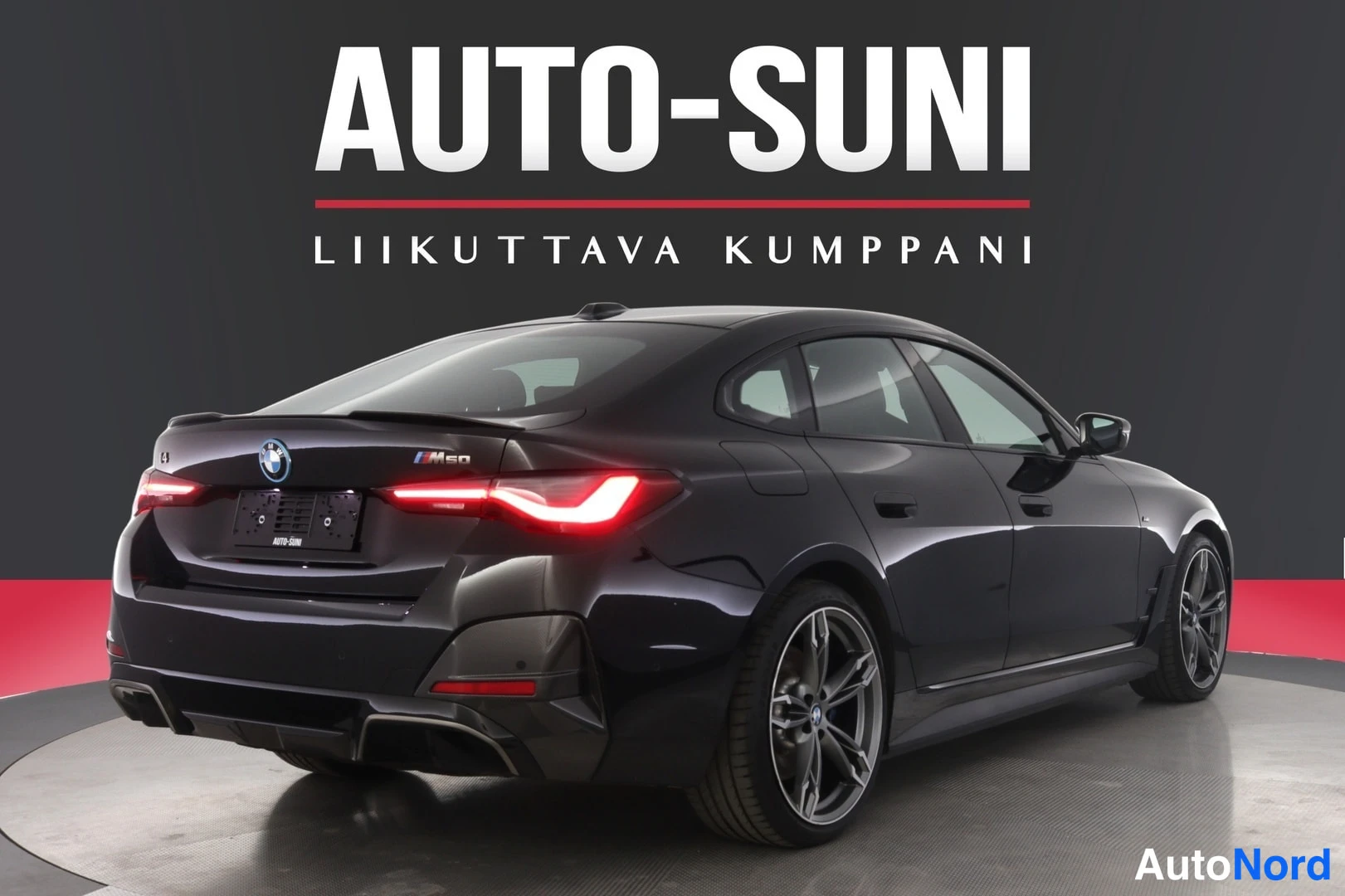 Takaviisto: Musta BMW i4 -sedan takaviistokulma studiosta, takavalot ja kannen M50-merkki näkyvissä.