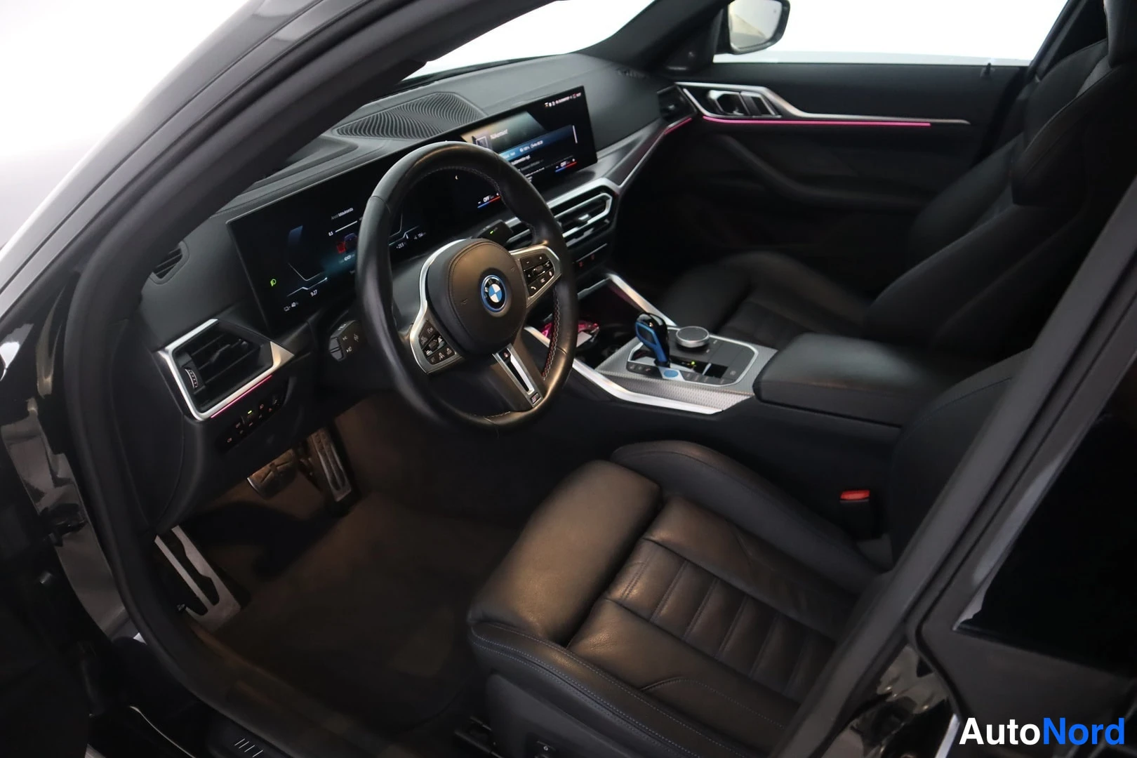 Muu: Kuljettajan puolen matkustamo vasemmalta: BMW-merkkinen ohjauspyörä, pitkä infotainment-näyttö kojelautana, automaattivaihteiston valitsin ja mustat nahkaistuim
