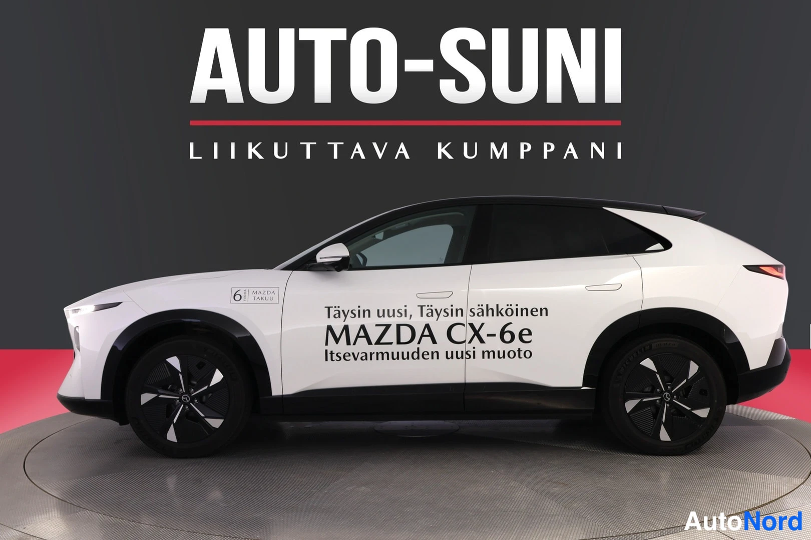 Sivulta: Valkoinen Mazda CX-6e sivusta kuvattuna, tummat pyörät ja katto, markkinointitekstit ovissa.