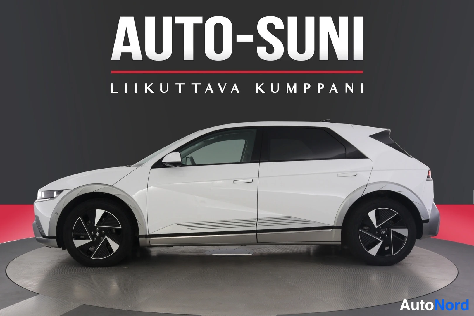 Sivulta: Auton kylki sivusta valokuvaus: valkoinen Hyundai-suvu tummissa vanteisilla pyörillä studio­taustaa vasten.