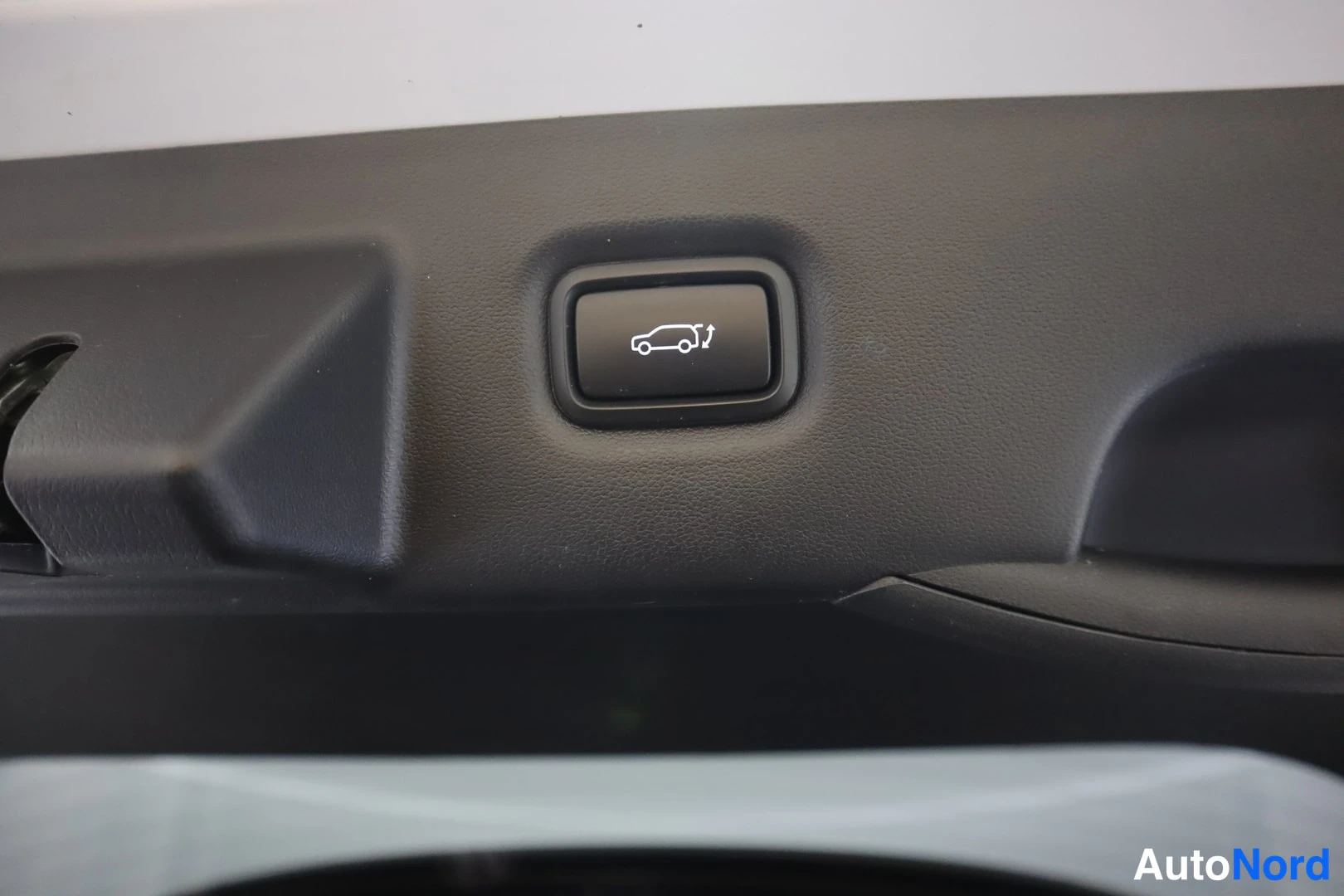Yksityiskohta: Suljettu tumma nappi, jonka ikonissa auto ja aukeava takaluukku, joko takaluukun aukaisun tai sulkemisen ohjaus.