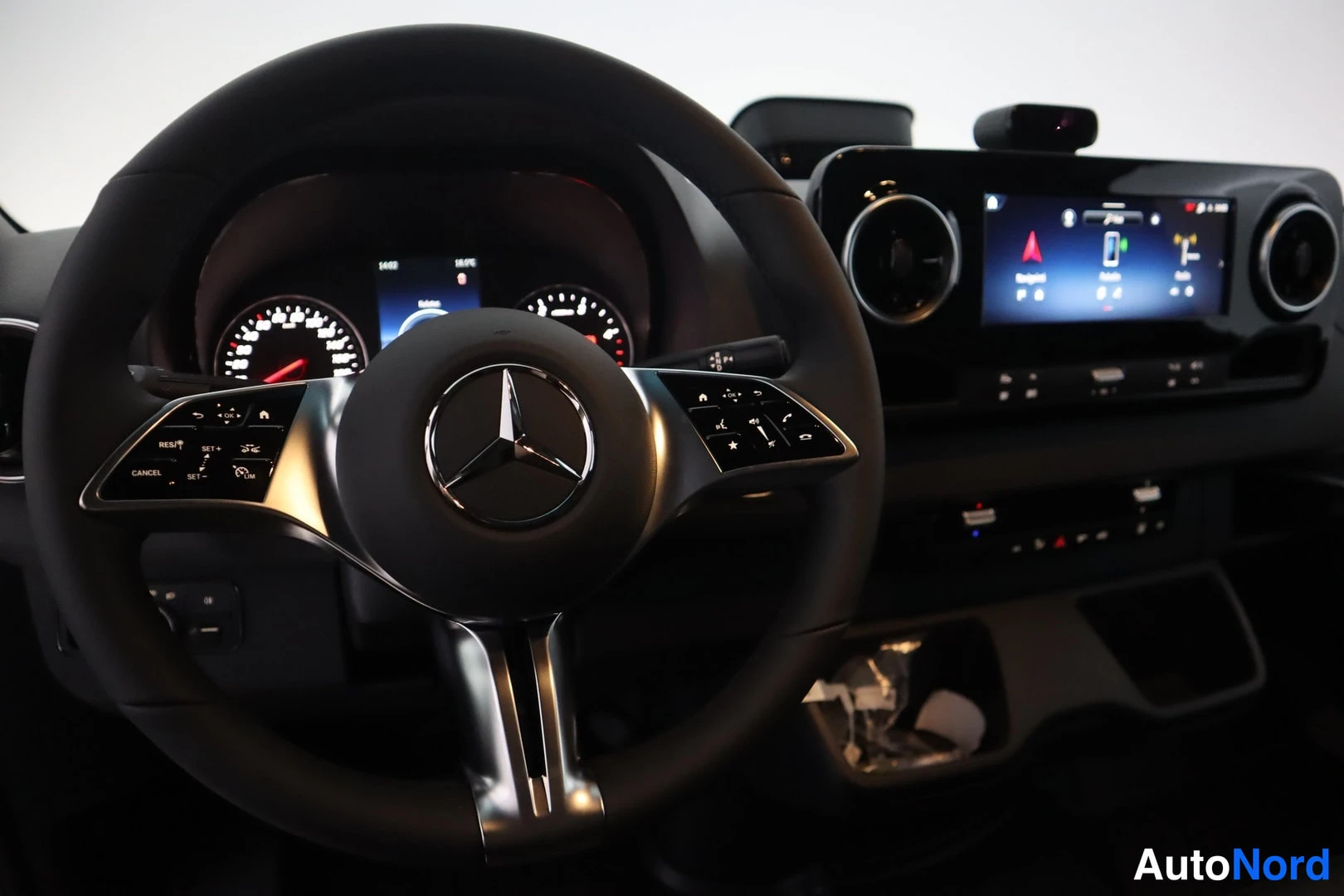 Muu: Ohjauspyörän lähikuva Mercedes-tunnuksella, takana mittaristo ja keskinäyttö.