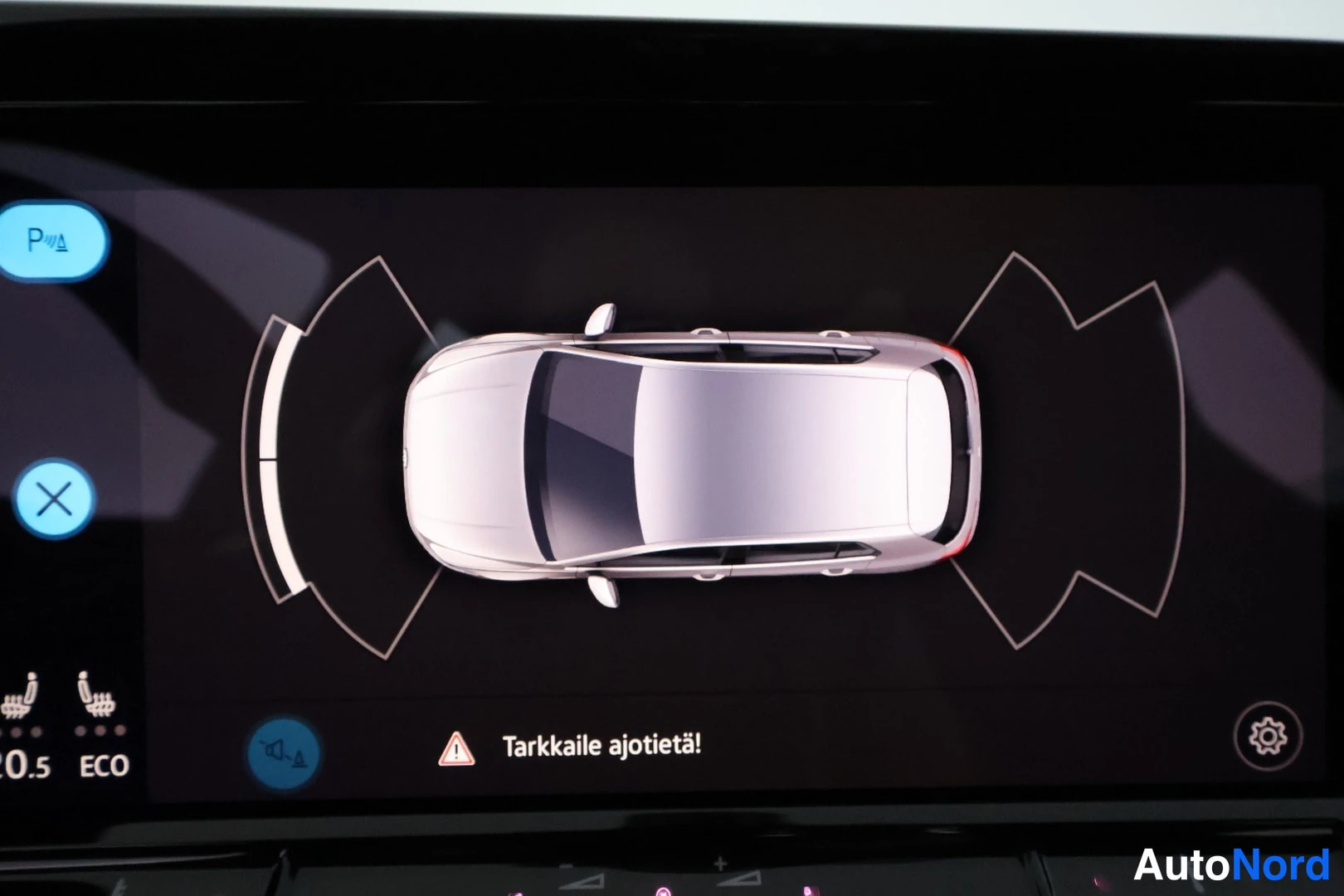 Yksityiskohta: Auton infotainment-näyttö, jossa parkkitutkan ympyräkaavio ja teksti 'Tarkkaile ajotietä!'