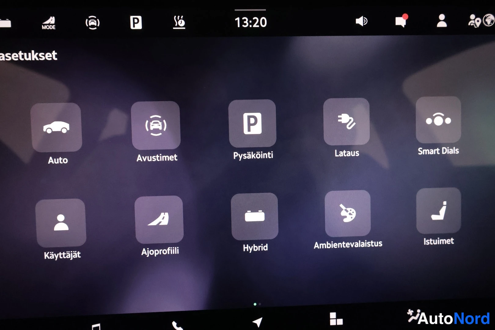 Ohjaamo: Ruudussa olevat asetukset-valikon ikoneja ovat Auto (Auto), Avustimet (Avaimet), Pysäköinti (Parkki), Lataus (Lataus), Smart Dials (Sähkövaihtimet). Toisella ri