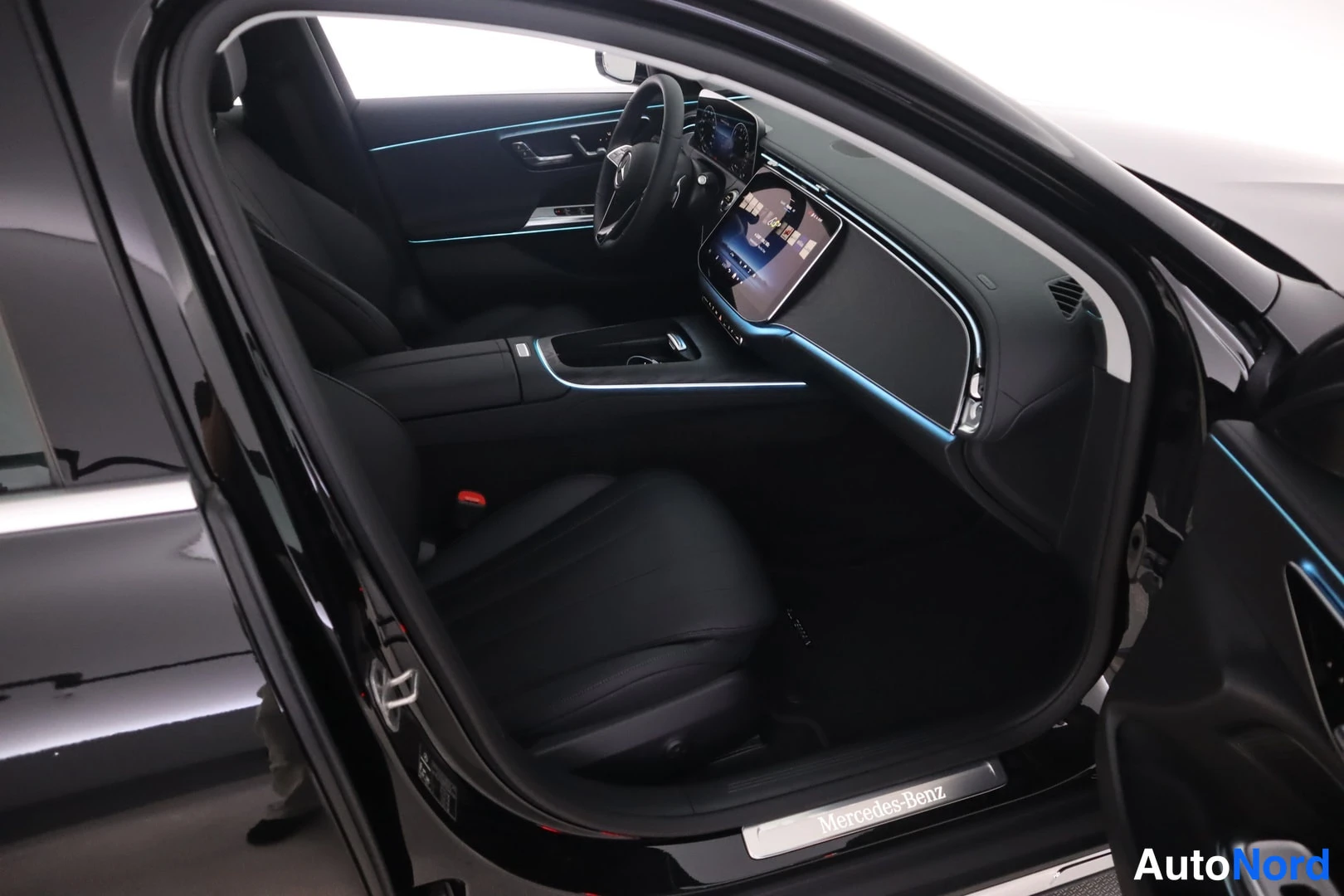 Yksityiskohta: Mustan Mercedes-Benzin kuljettajan oven auki: mustat nahkaiset etuistuimet, ohjauspyörä, keskinäyttö, tunnelmavalaistus ja ovikynnöksellä Mercedes-Benz-teksti.